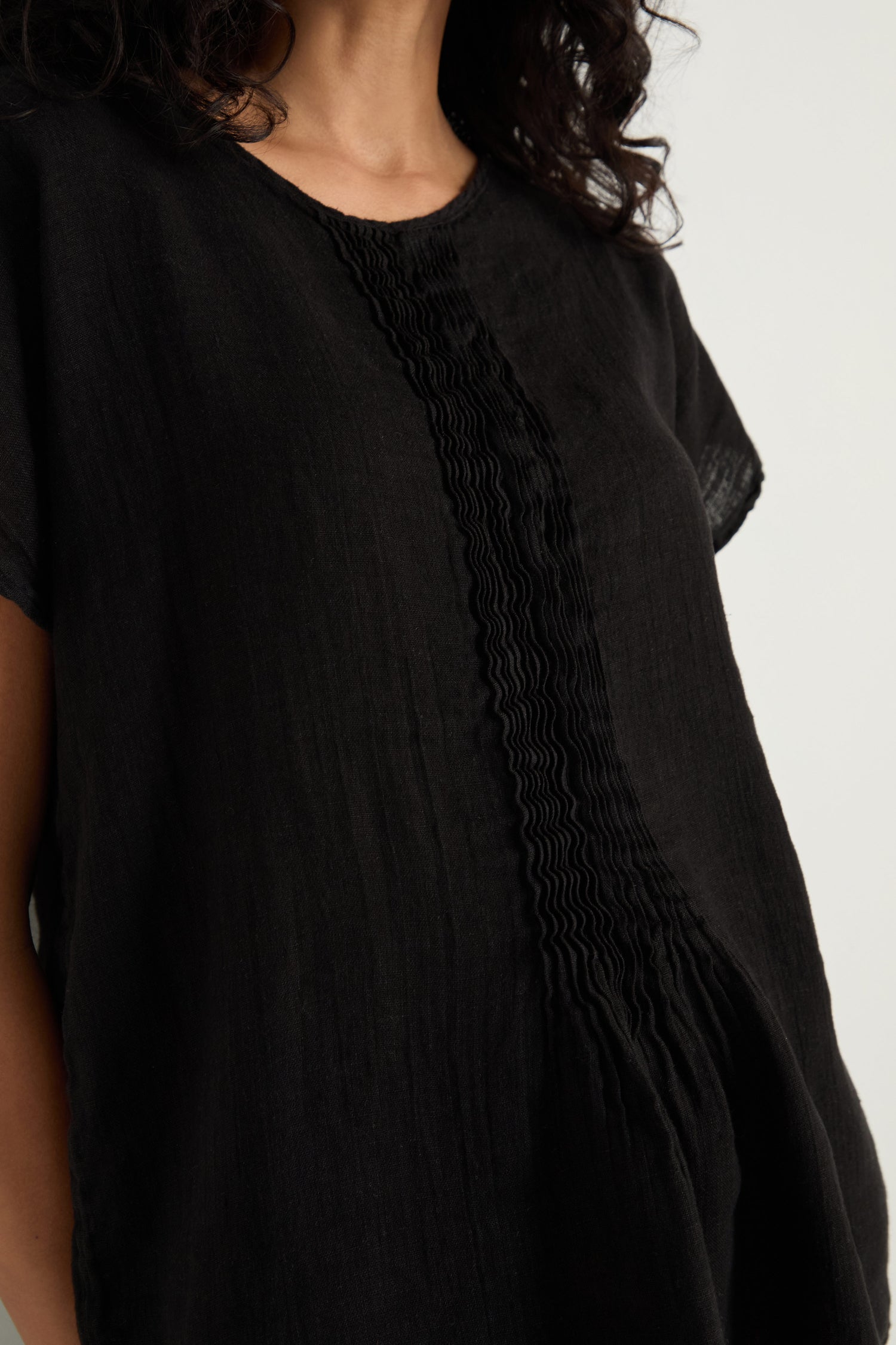 Someone wearing the Pleat Front Linen Top in black, featuring vertical detailing and a relaxed silhouette.