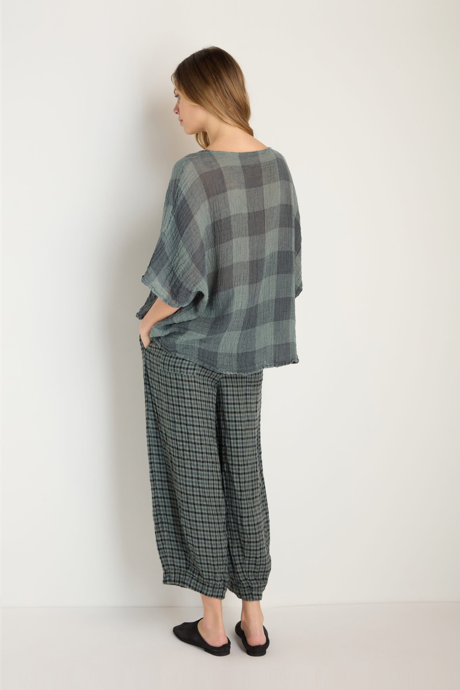 A woman faces away from the camera, wearing the Large Check Boxy Top and matching pants with black slip-on shoes against a plain light background.