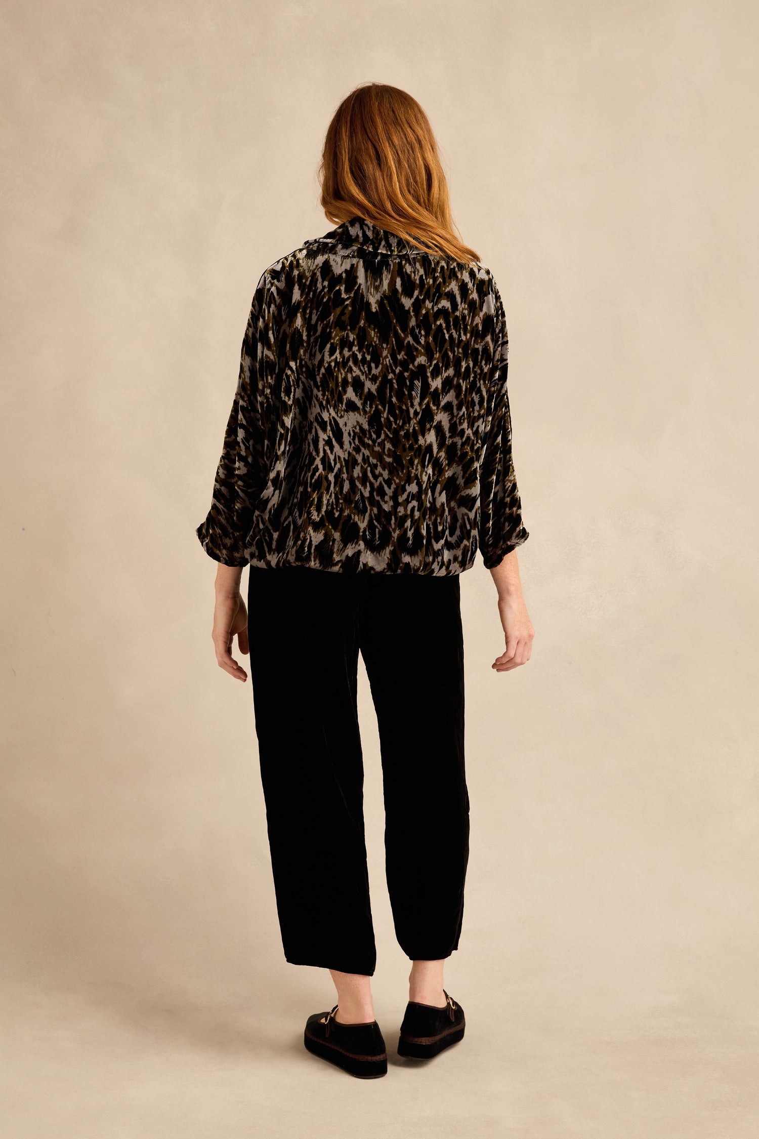 A person with long hair is seen from behind, wearing a patterned jacket layered over the Animal Print Cowl Neck Velvet Top, paired with black pants and black shoes, standing against a neutral background.
