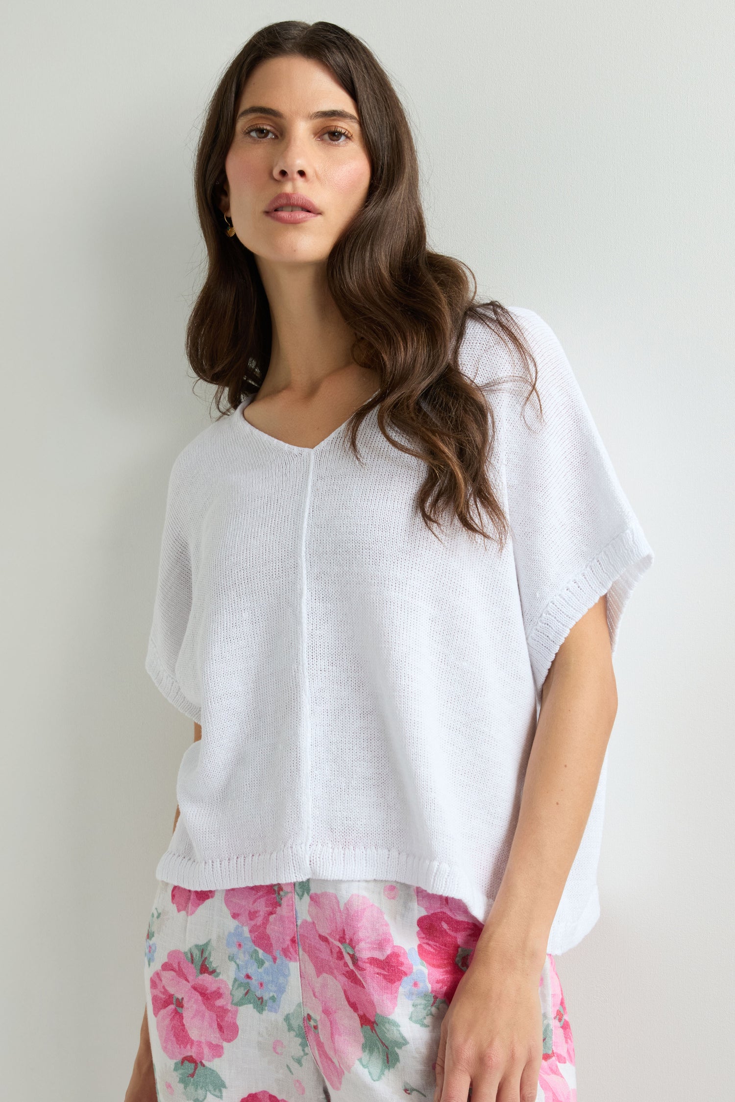 Woman in a loose Sleeveless V Neck Boxy Linen Knit top and white shorts with a pink floral pattern, standing against a plain light background.