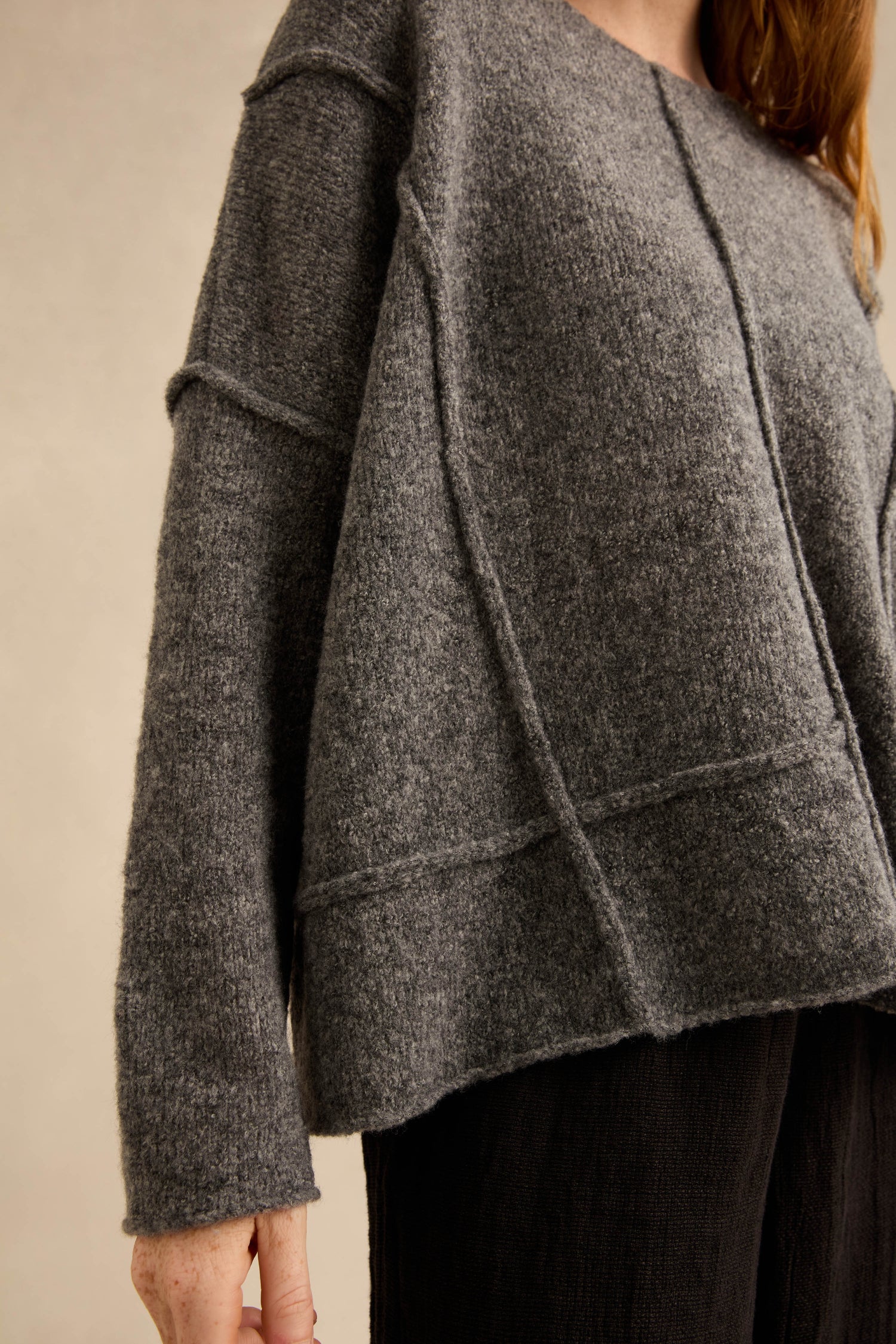 Wearing the Grey Seamed Knit—a loose-fitting, textured gray sweater featuring visible curved seam detailing and long sleeves—paired with dark pants.