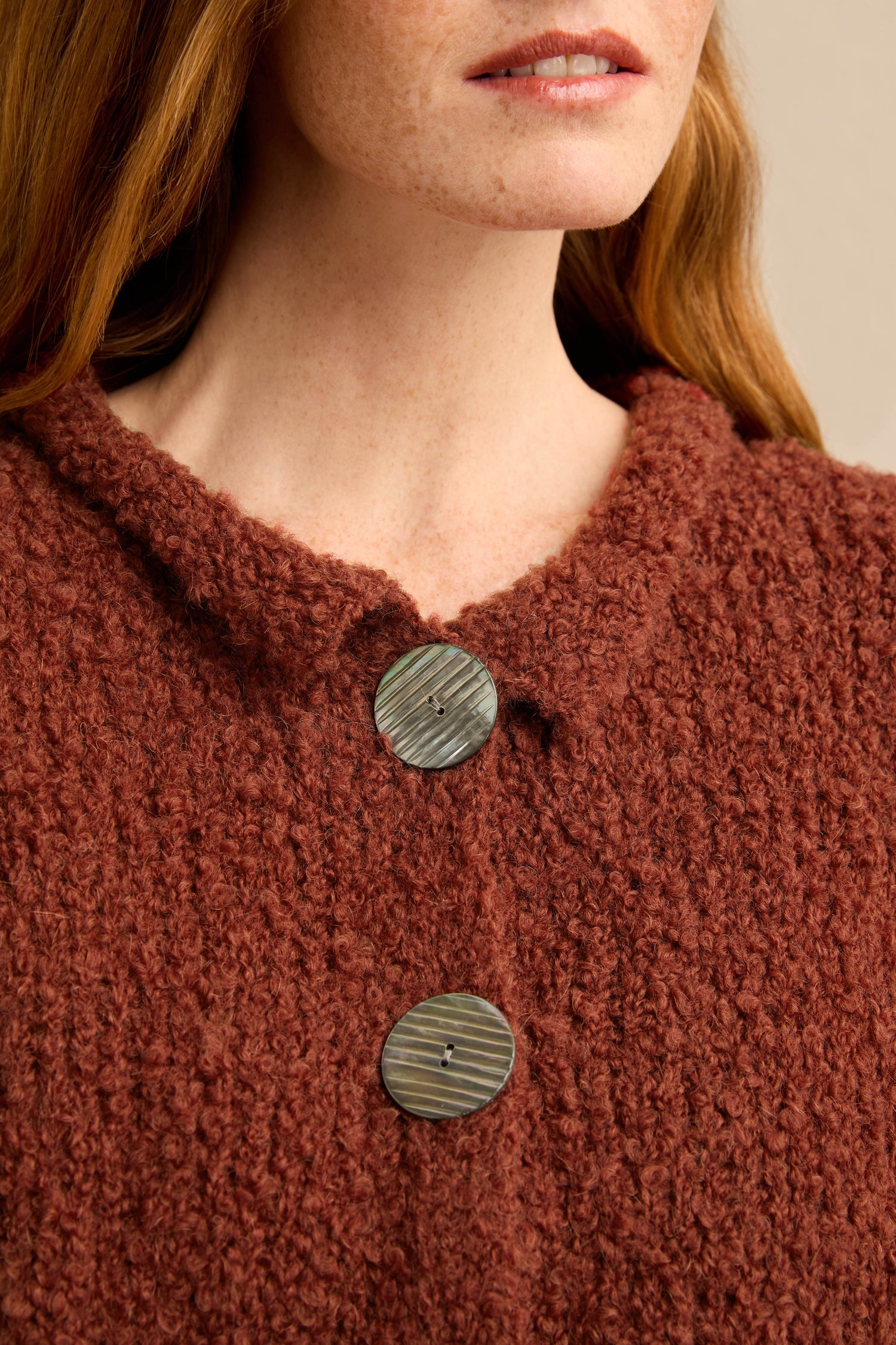 Close-up of a person wearing the Three Button Cardigan, a textured, burgundy oversized sweater featuring large, round buttons; only the lower face and upper torso are visible.