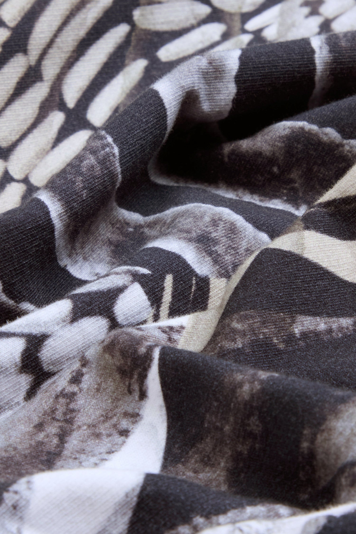 Close-up of black, white, and beige patterned fabric with a slightly wrinkled texture and organic shapes resembling scales or feathers, characteristic of the pure cotton Monochrome Patchwork Jersey Jacket.