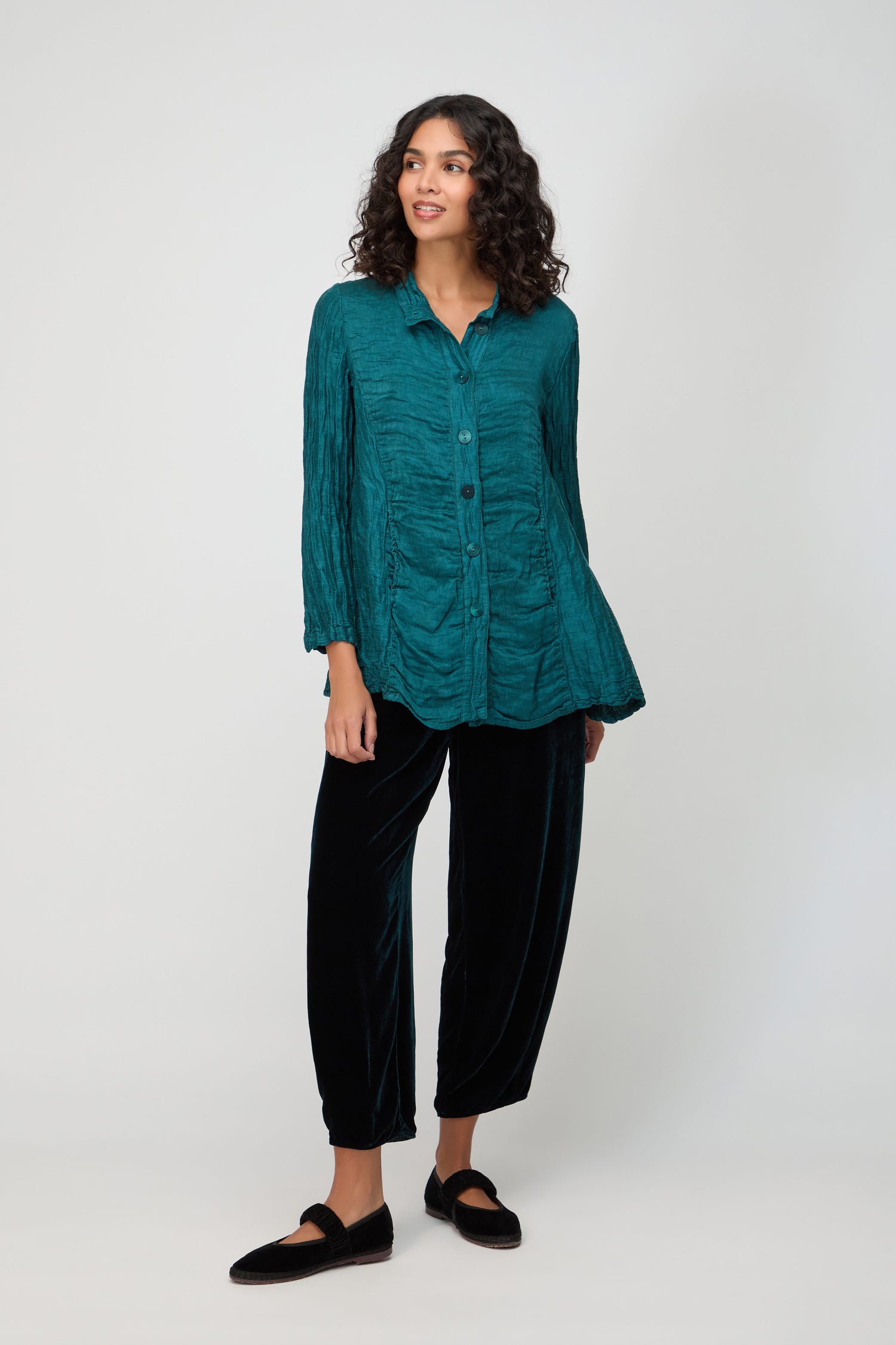 A woman stands against a plain background wearing a teal Panel Front Silk Linen Jacket, black loose pants, and black loafers. She gazes slightly to the side with a neutral expression.
