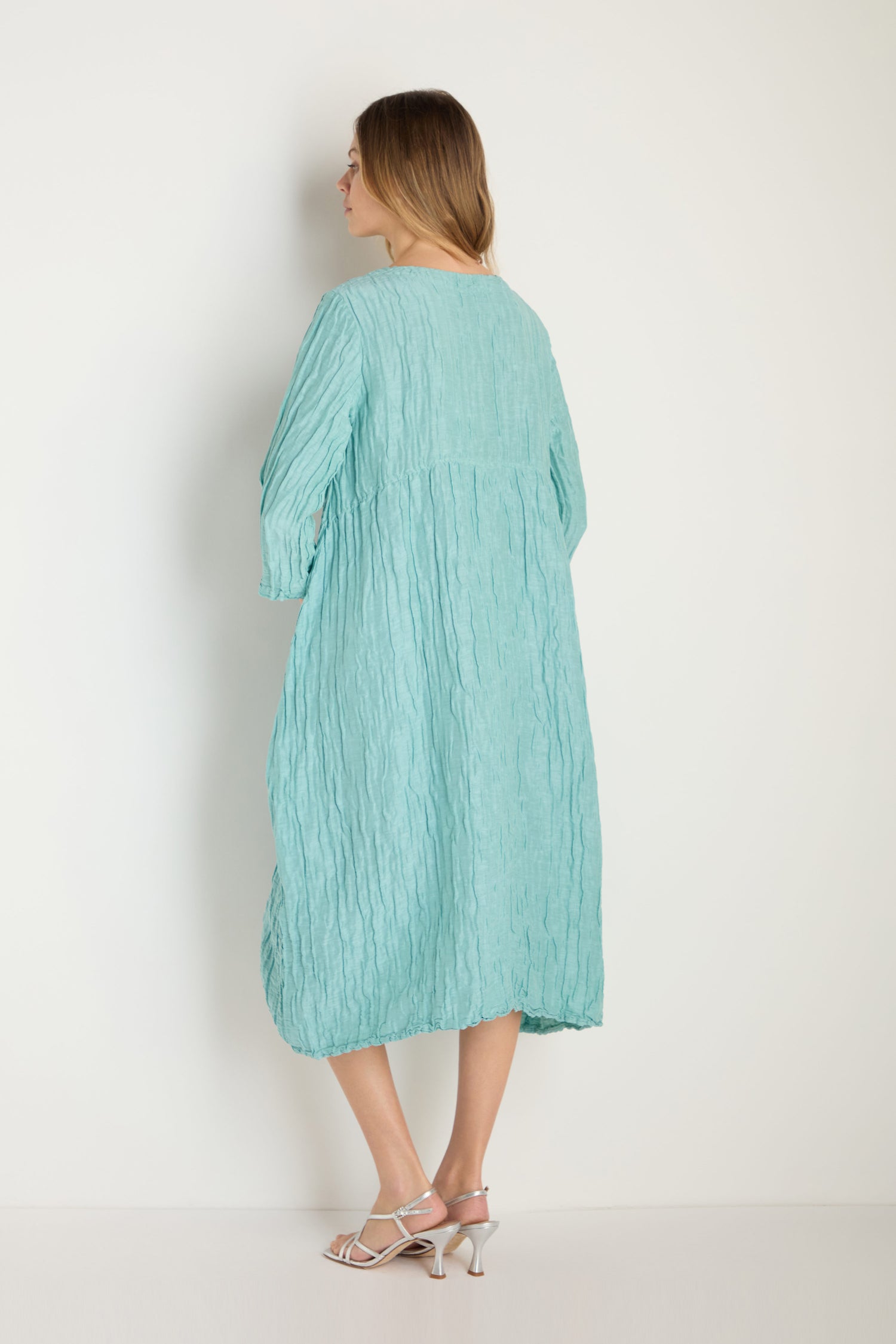 A woman faces away from the camera, wearing the Silk Linen Mint Patch Pocket Dress and white heeled sandals, set against a plain light background.