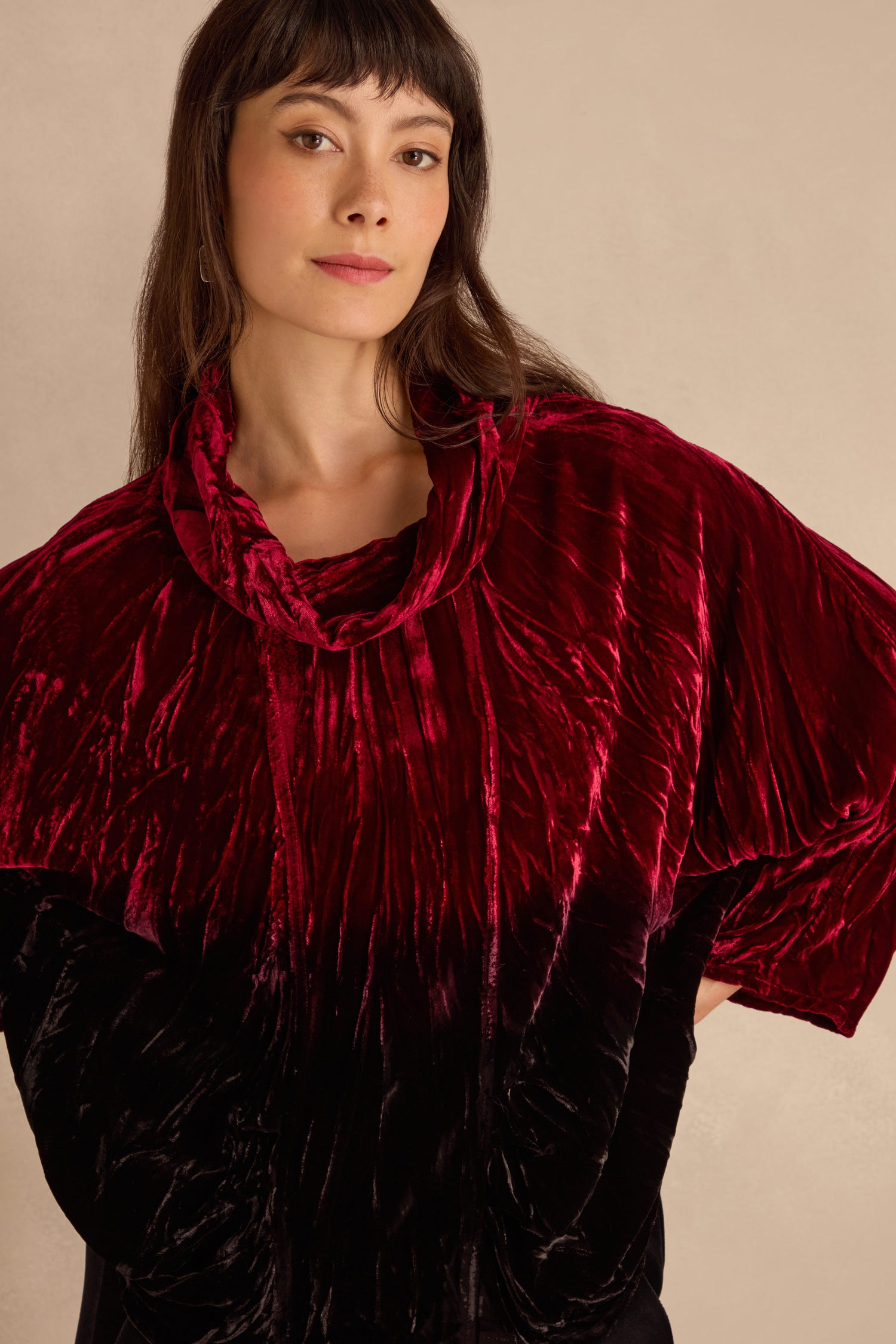 Woman wearing the Ruby Silk Velvet Ombre Cowl Neck Top, a loose dark red velvet piece, against a plain beige background.