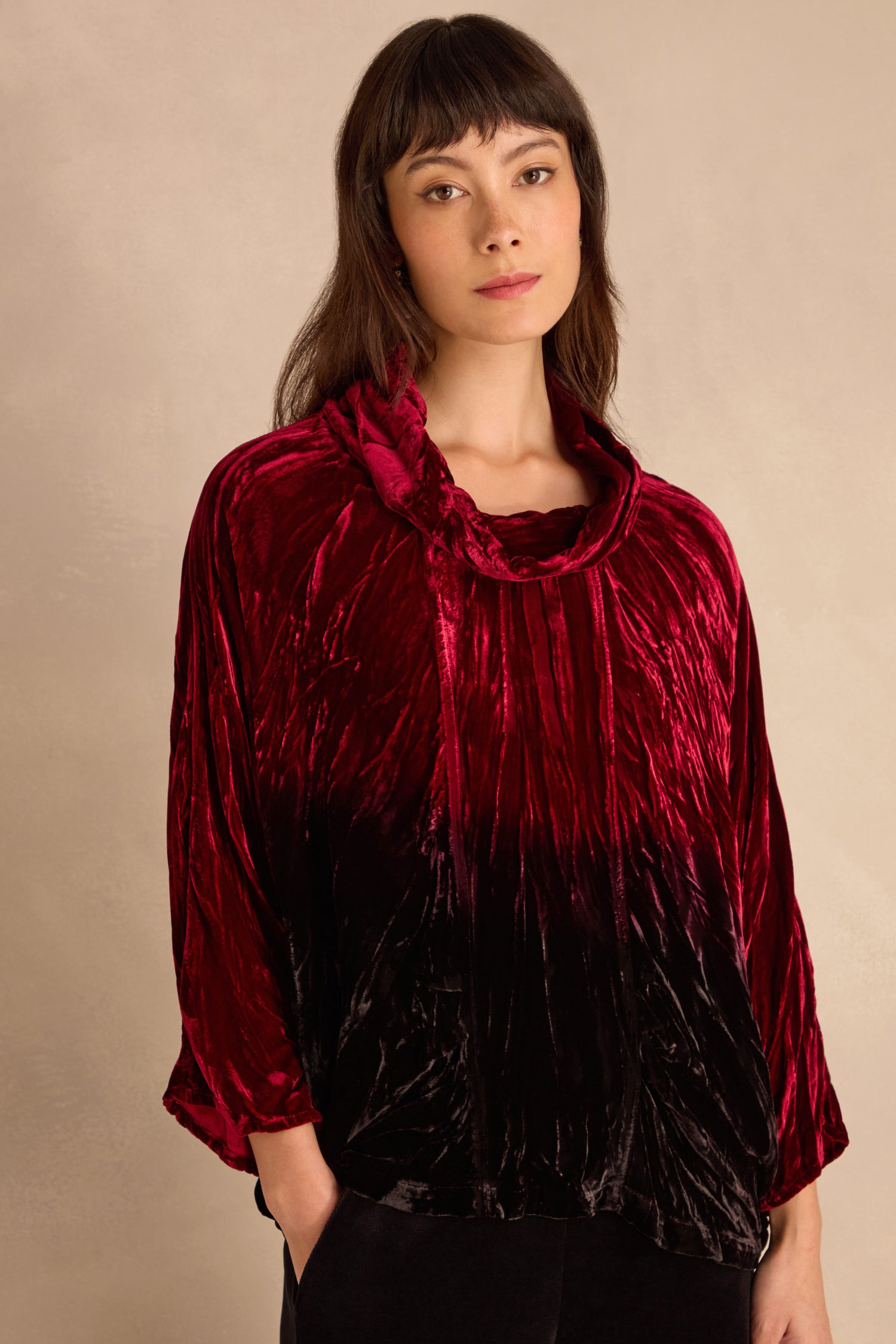Woman wearing the Ruby Silk Velvet Ombre Cowl Neck Top, featuring a loose fit and ombre red and black velvet, against a neutral background.