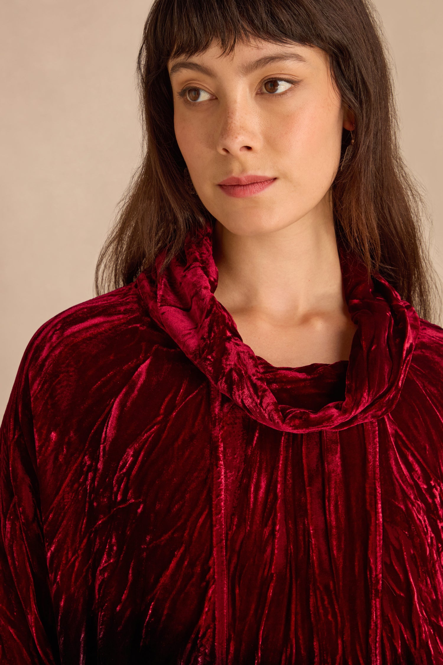 A woman with long brown hair wears the Ruby Silk Velvet Ombre Cowl Neck Top in deep red, gazing slightly to the side.