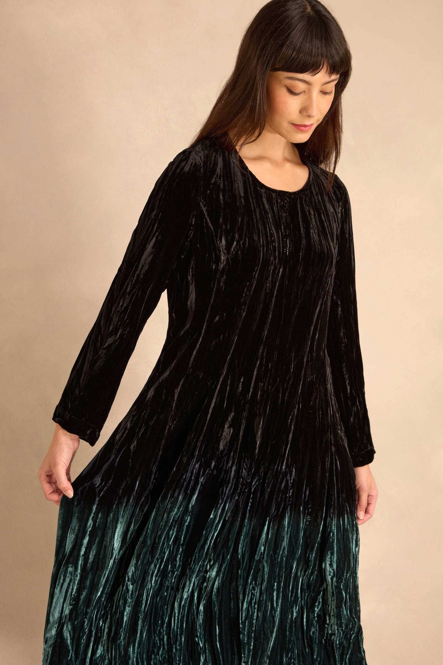Woman wearing the Silk Velvet Ombre Bubble Dress, featuring long sleeves and ombre shading that fades into green at the hem, looking down with one arm slightly extended.