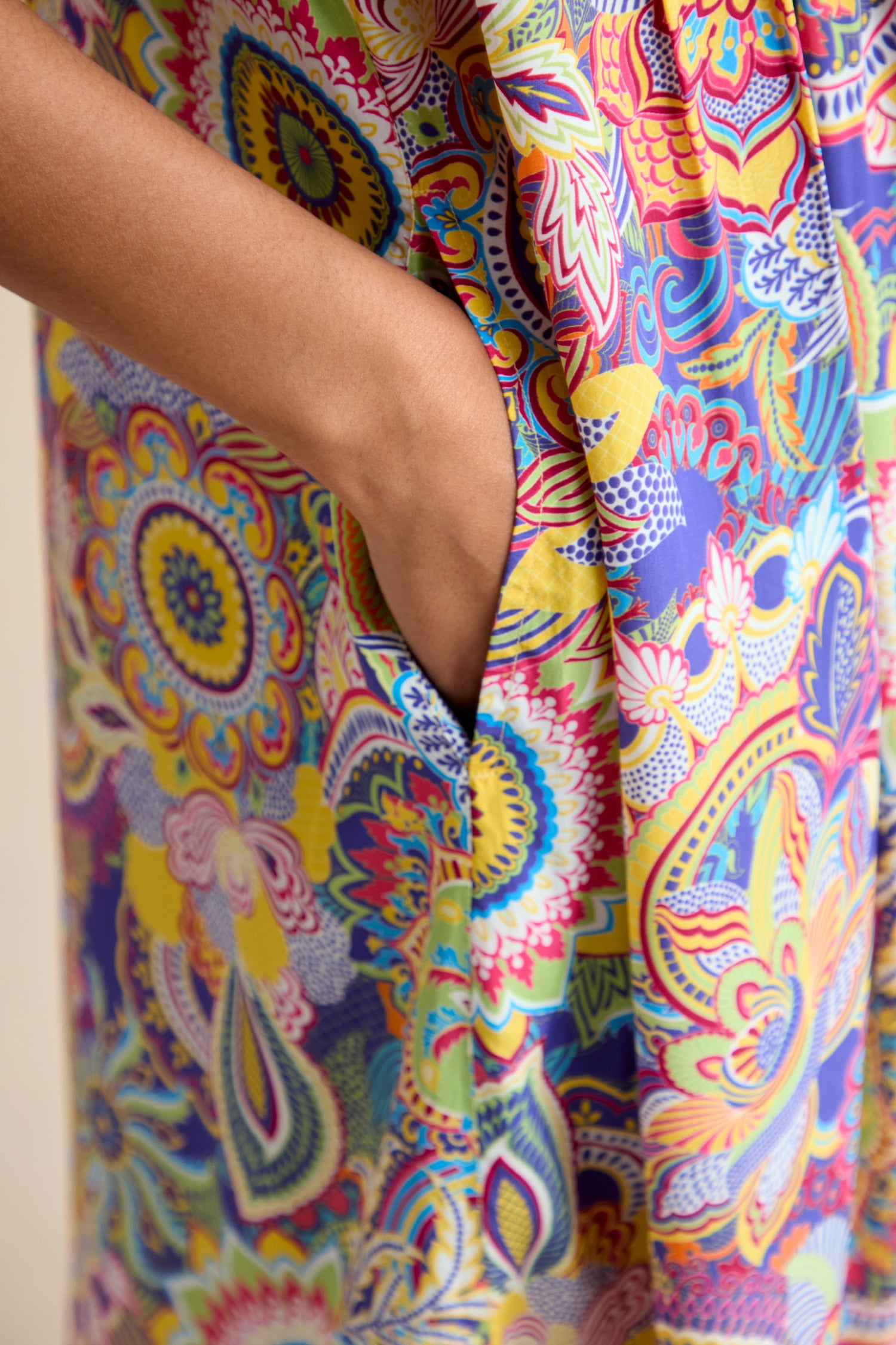 A close-up of a person's hand in the pocket of the Summer Sarasa Jumpsuit, a colorful, patterned silk-like viscose piece featuring intricate floral and paisley designs.