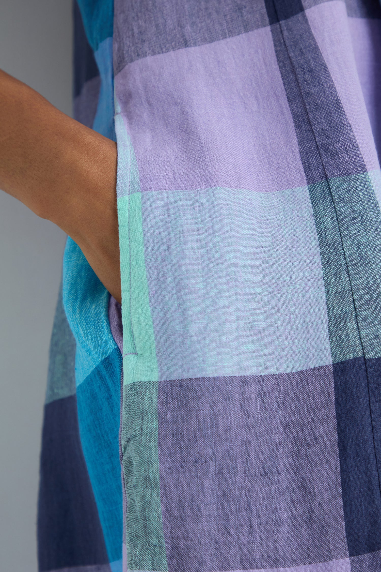 Close-up of a person's hand in the pocket of the Cross Dye Check Linen Bubble Dress, featuring a blue, purple, and teal plaid pattern.