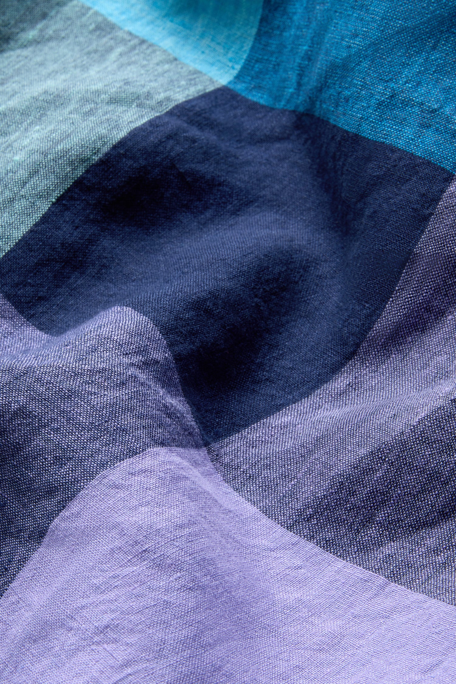 A close-up of crumpled fabric from the Cross Dye Check Linen Maxi Dress, showcasing its v-neck design and irregular blue and purple color blocks.