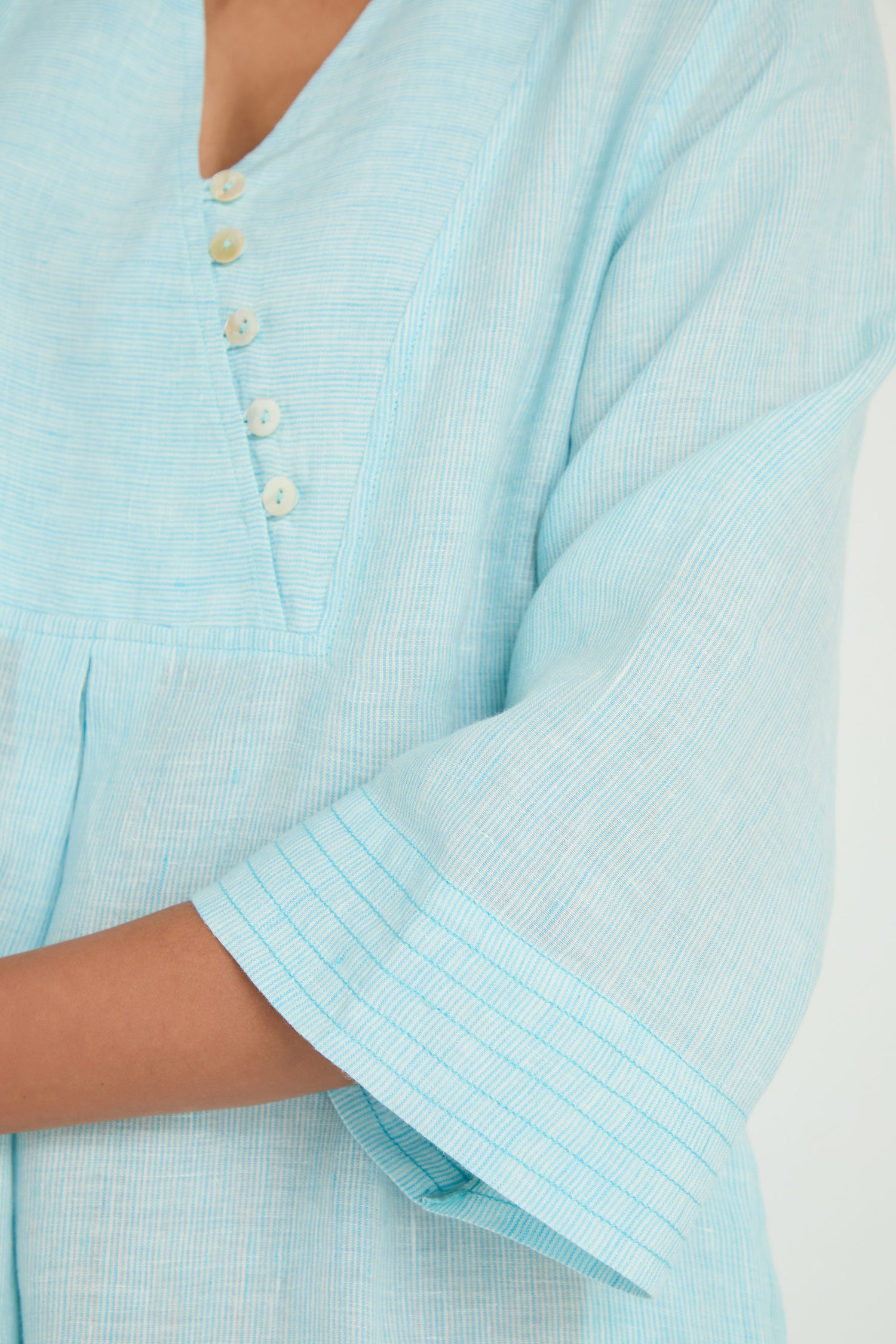 Close-up of a person wearing the Ticking Stripe Linen Button Placket Dress, featuring light blue stripes, a V-neck, button placket, and an A-line silhouette inspired by classic linen stripe dresses.