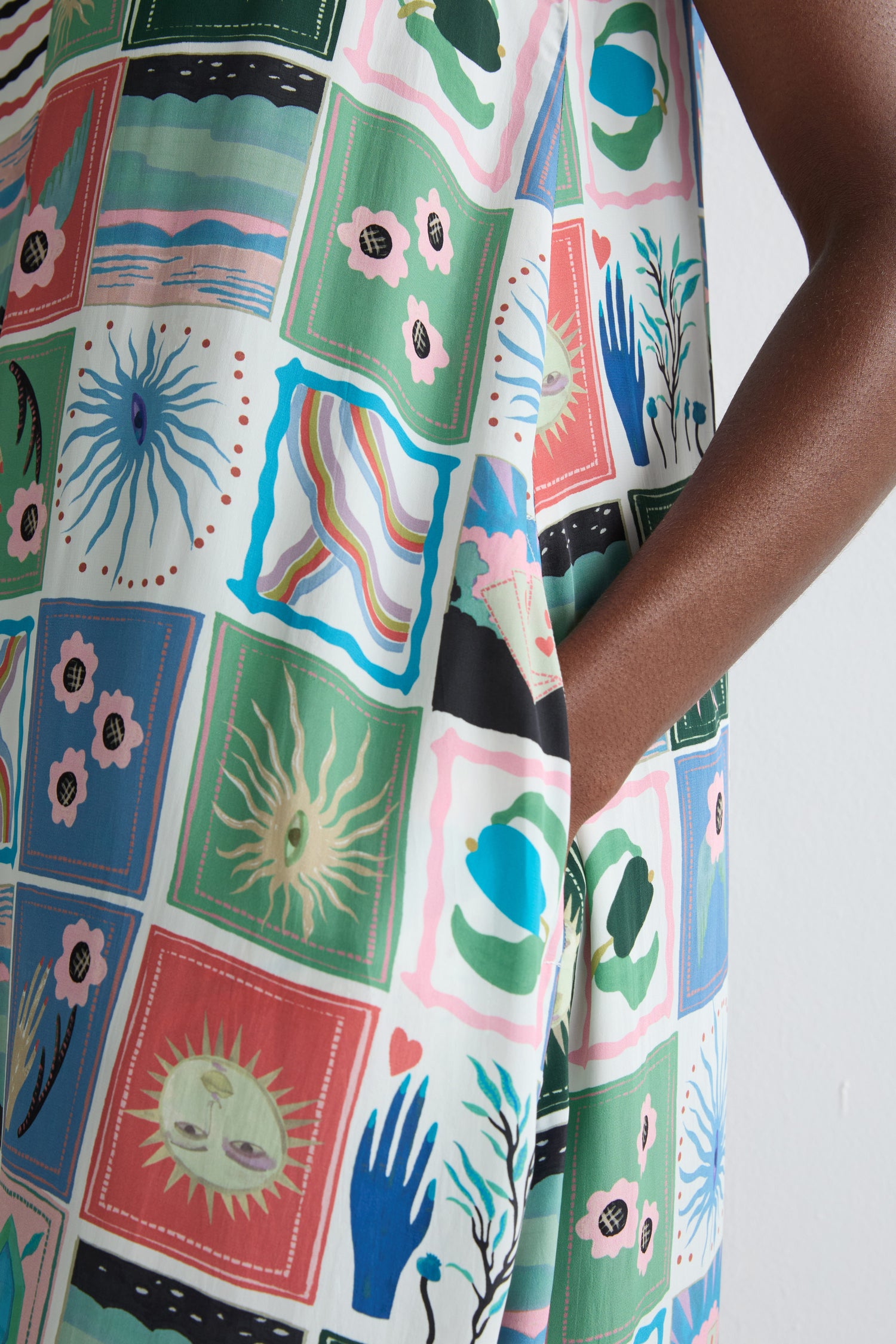 Wearing the Mystical Collage Sleeveless Dress, a vibrant patchwork of abstract and nature-inspired prints, a person stands against a plain white background.