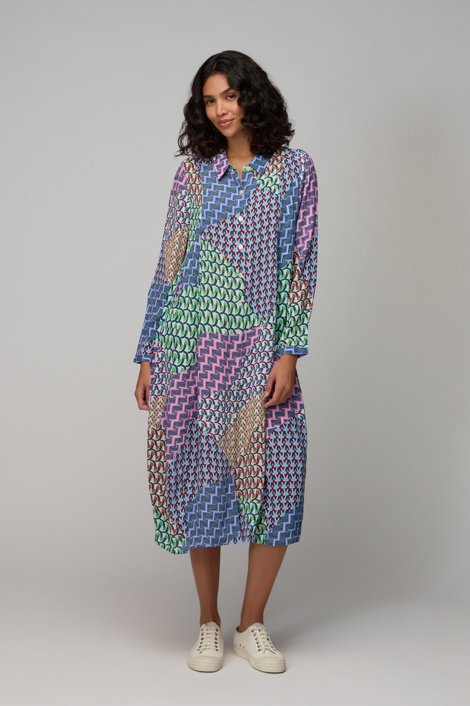 A woman wears the Geo Patchwork Print Shirt Dress, featuring a colorful geometric pattern and long sleeves, standing against a plain light gray background.