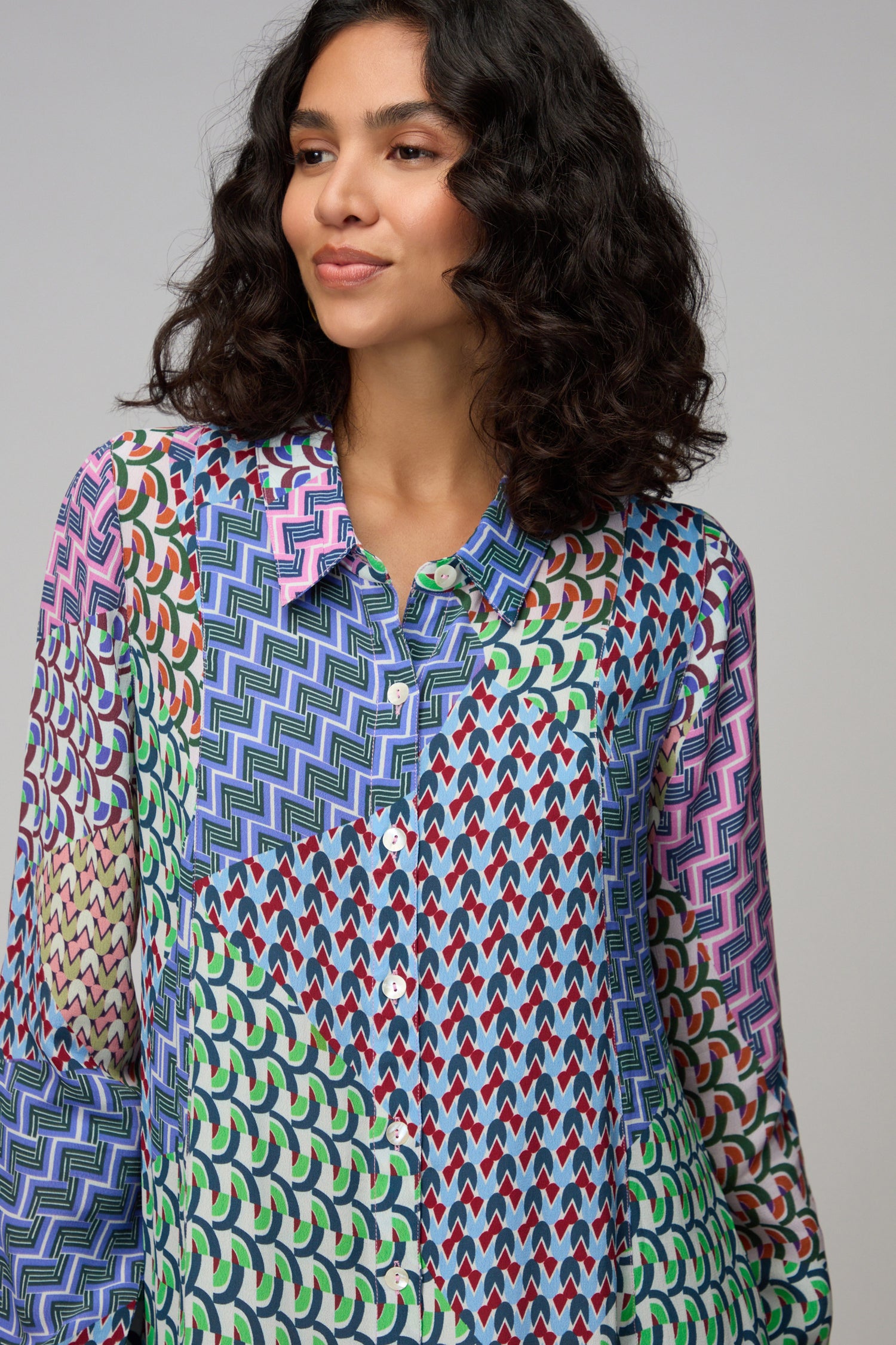 A woman with dark curly hair tied back models the Geo Patchwork Print Shirt Dress, gazing slightly away from the camera against a plain backdrop.
