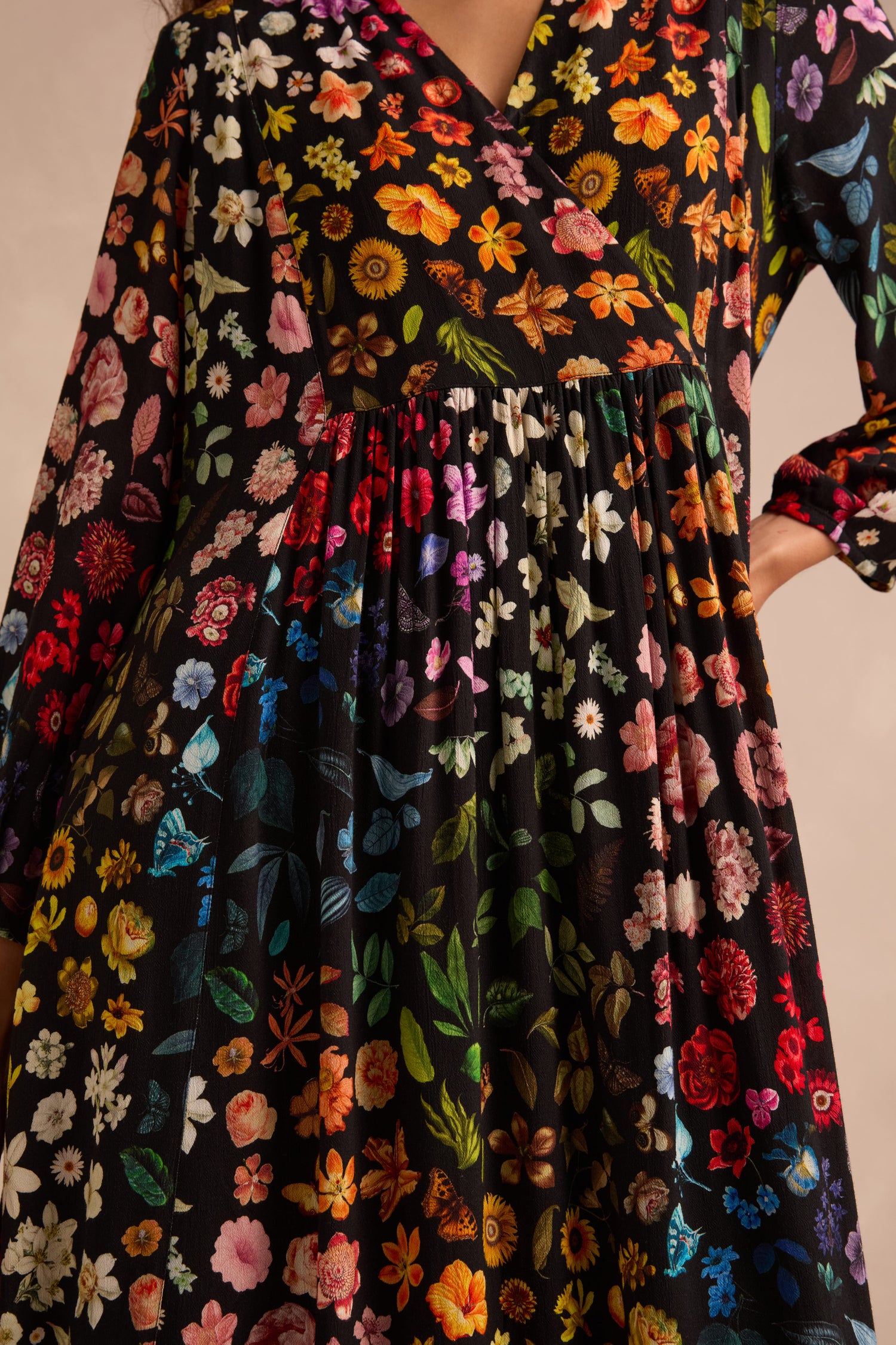 A woman wearing the Midnight Garden Viscose Dress—a long-sleeved black dress featuring a colorful, vibrant floral pattern—shown from shoulders to knees with one hand on her hip.