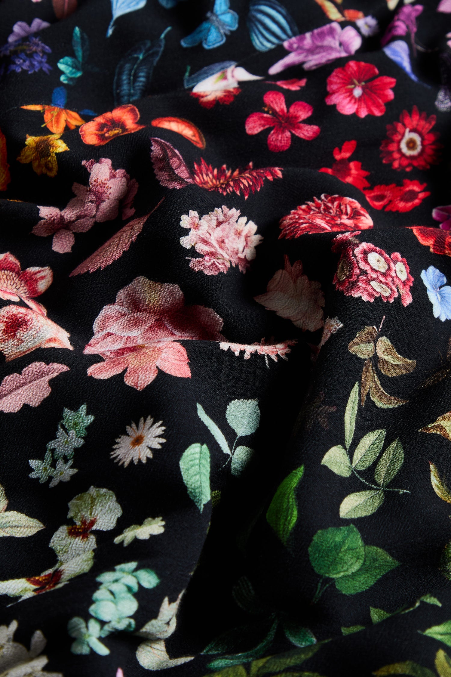 Close-up of the Midnight Garden Viscose Dress showcases black fabric adorned with colorful printed flowers and leaves, blending vibrant reds, pinks, greens, and blues on a dark background—ideal for crafting an elegant floral crepe dress or a stylish wrap front dress.