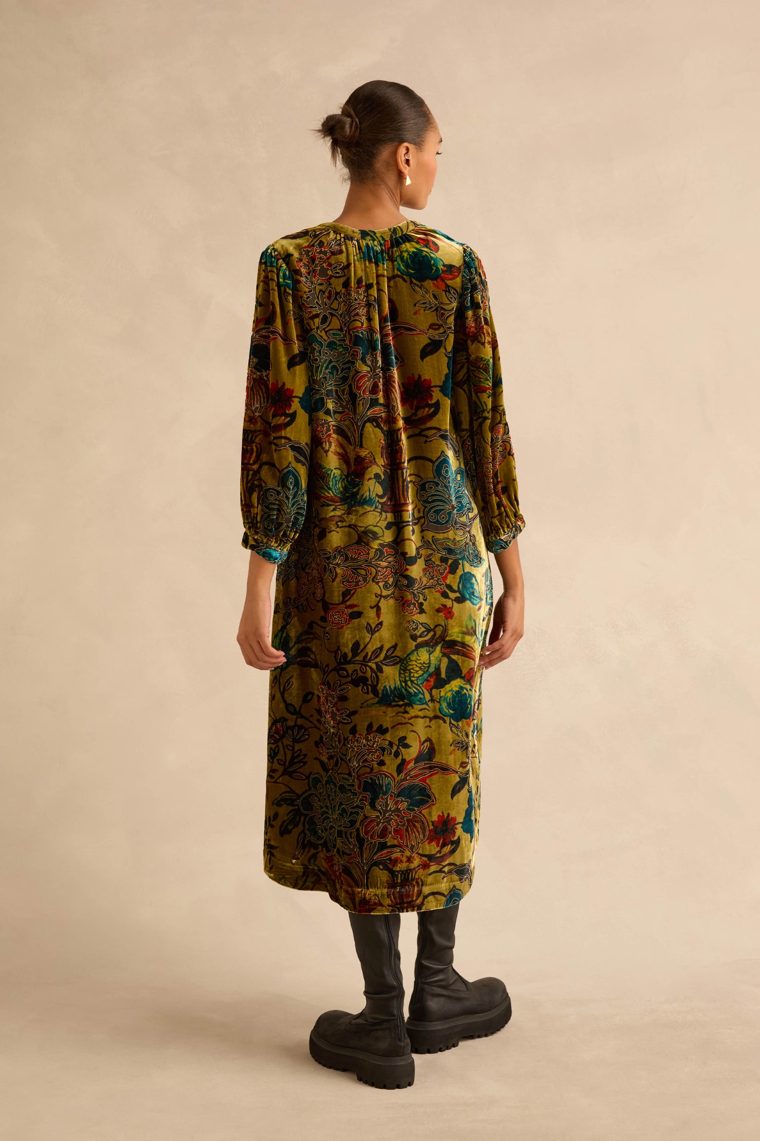 A model wears a long-sleeved, olive green Silk Velvet Floral Devore Dress in a midi length featuring a dark floral print and black platform boots.