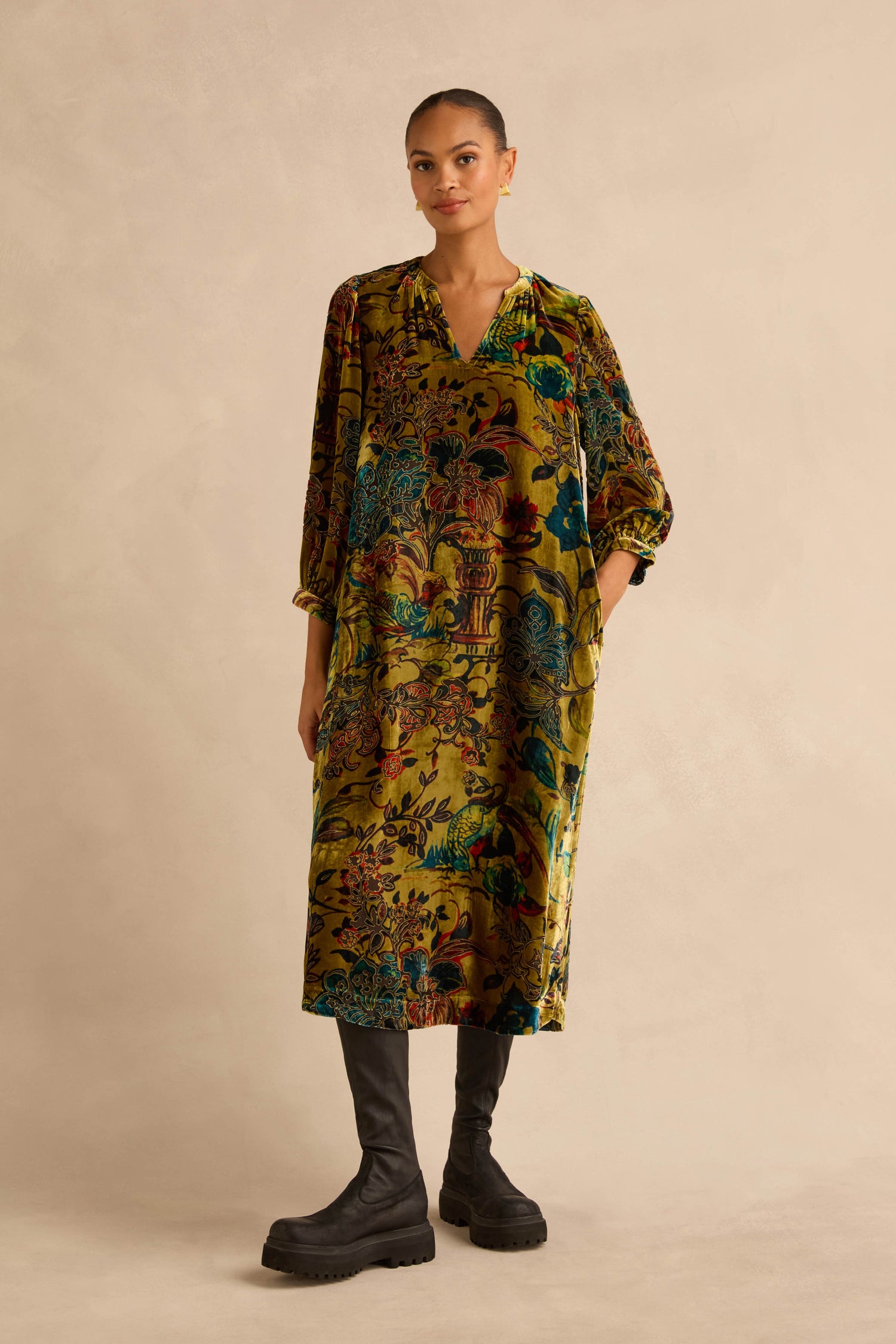 A woman wearing a knee-length, long-sleeved Silk Velvet Floral Devore Dress with a colorful floral pattern and black platform boots.