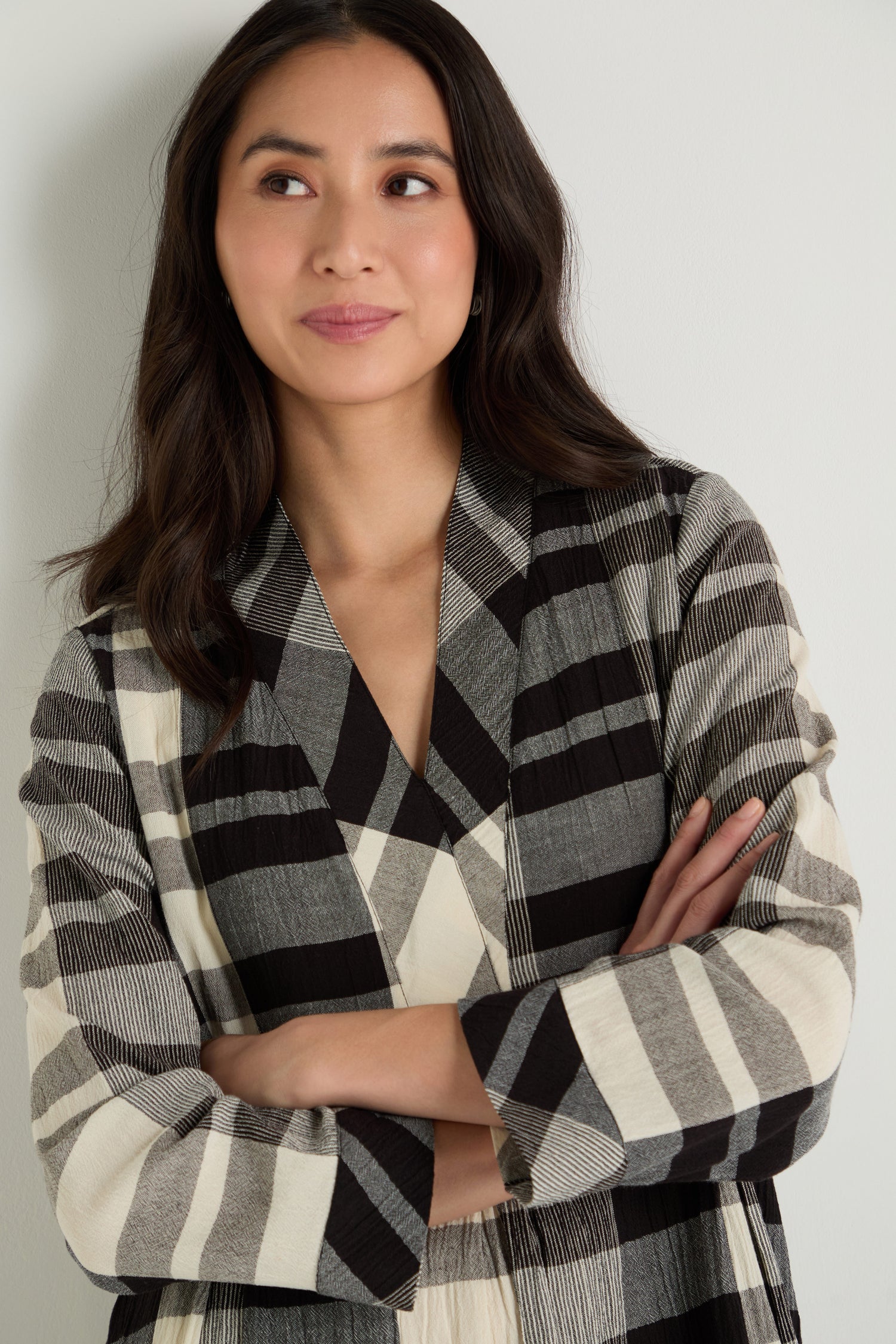 A woman stands against a plain light background wearing the Monochrome Crinkle Check Dress, a loose-fitting, long-sleeved piece with a bold black and white plaid pattern.