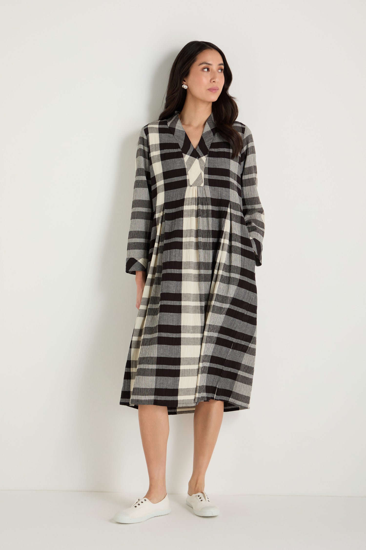 A woman with long dark hair sits against a plain background, wearing a loose-fitting Monochrome Crinkle Check Dress featuring a black and white plaid pattern.