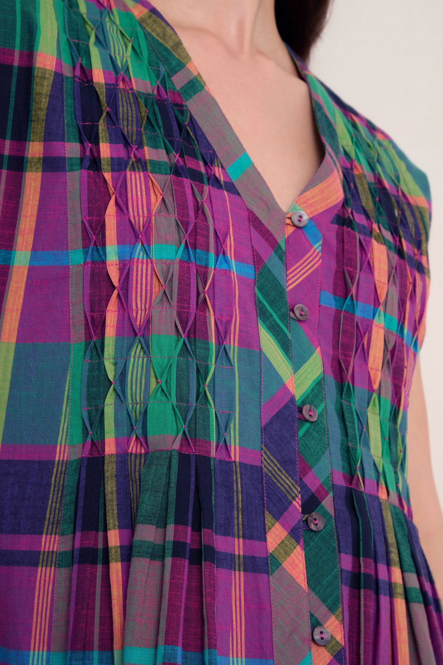 Close-up of the Madras Check Dress, a sleeveless pure cotton dress featuring a colorful Madras check pattern and diamond-shaped pleat details on the front.