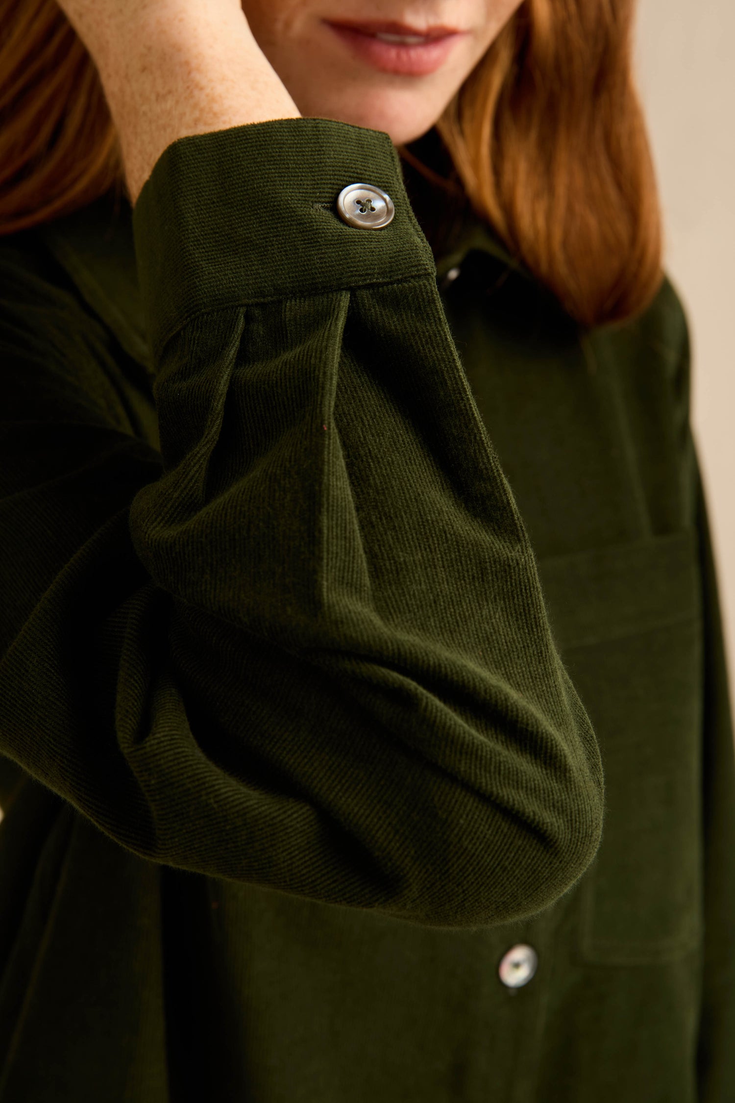 A person wearing the Forest Pinwale Cord Shirt Dress, featuring visible silver buttons and long sleeves. The image focuses on the shirt’s cuff and sleeve detail, showcasing the unique pinwale cord texture and tailored fit of this stylish cotton dress.