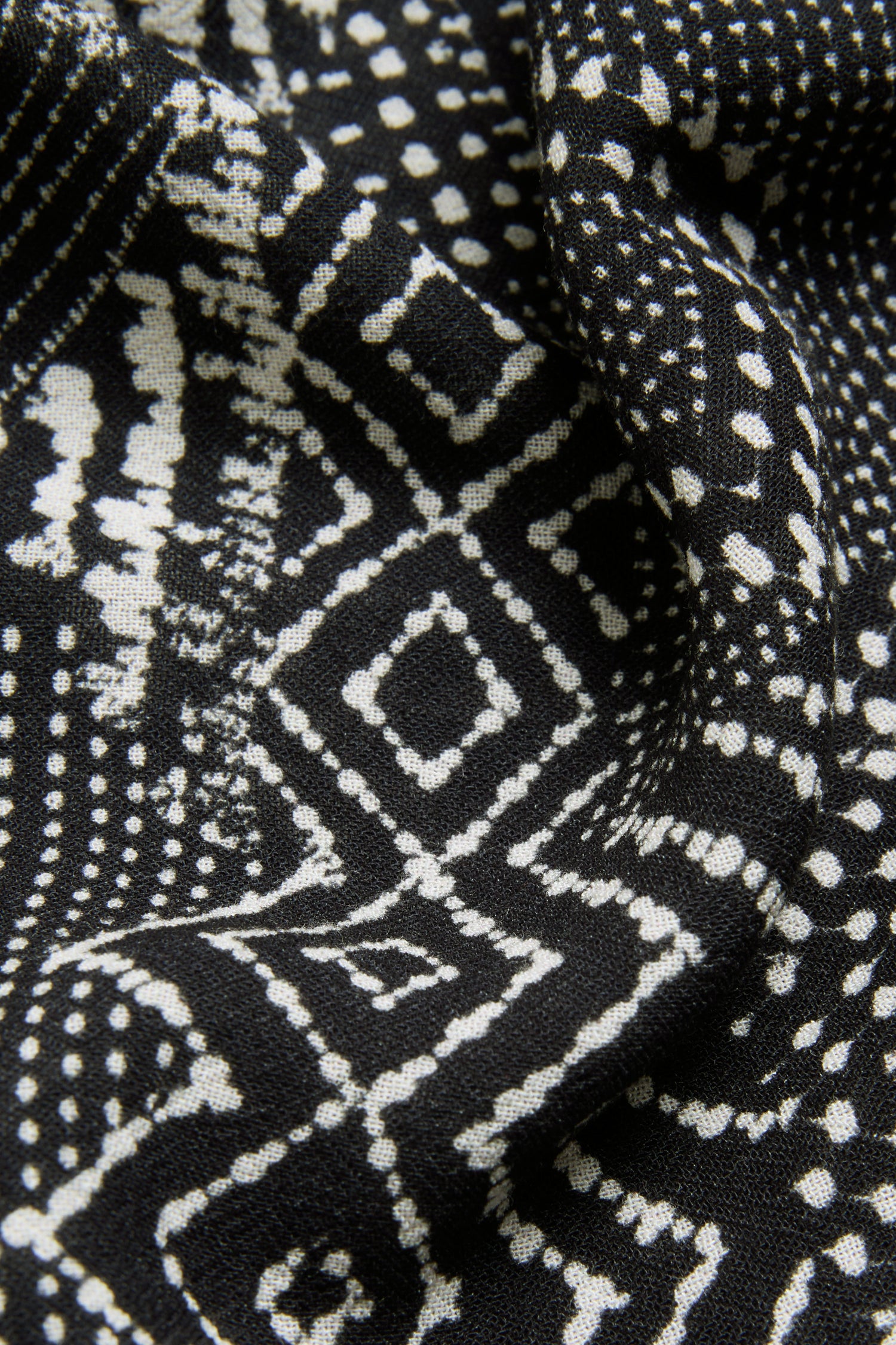 Close-up of the Mono Patchwork Ikat Dress fabric, showcasing white geometric patterns—including dots, diamonds, and lines—on a monochrome background with slight folds that enhance its textured appearance.