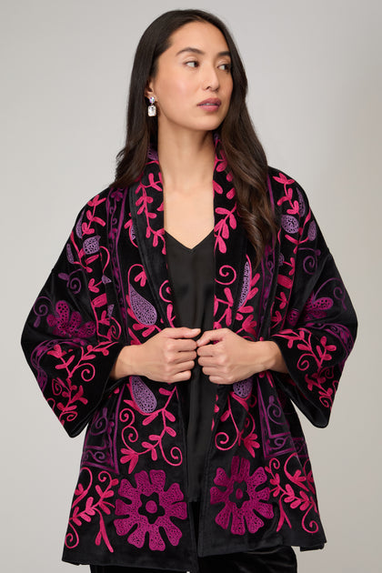 A woman with long dark hair models the Winter Embroidered Jacket, featuring black and magenta floral embroidery, over a black outfit against a plain background—ideal for stylish winter wear.