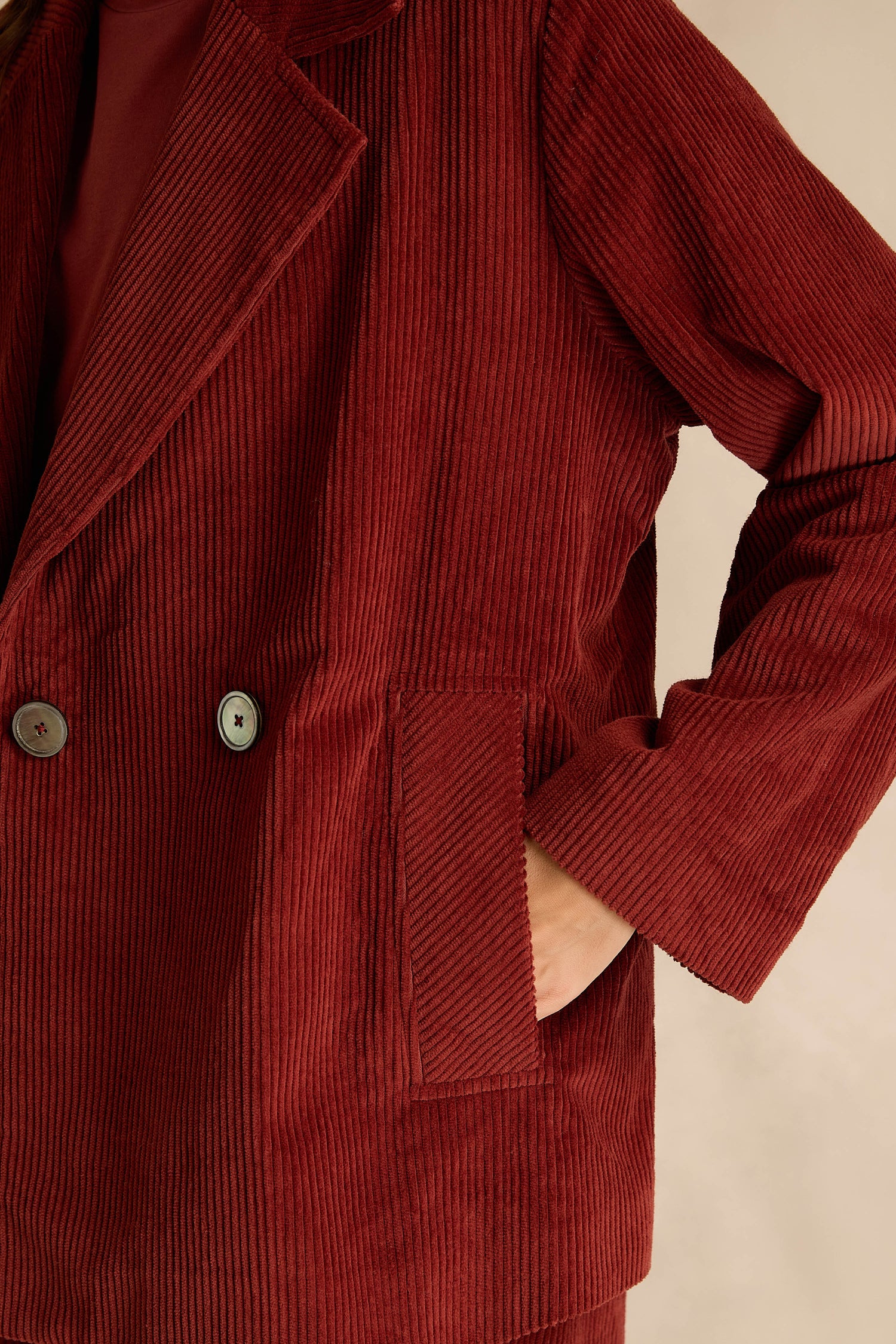 Close-up of a person wearing the Conker Jumbo Cord Caban Jacket, a red broad wale cord blazer with two buttons and one hand in the pocket.