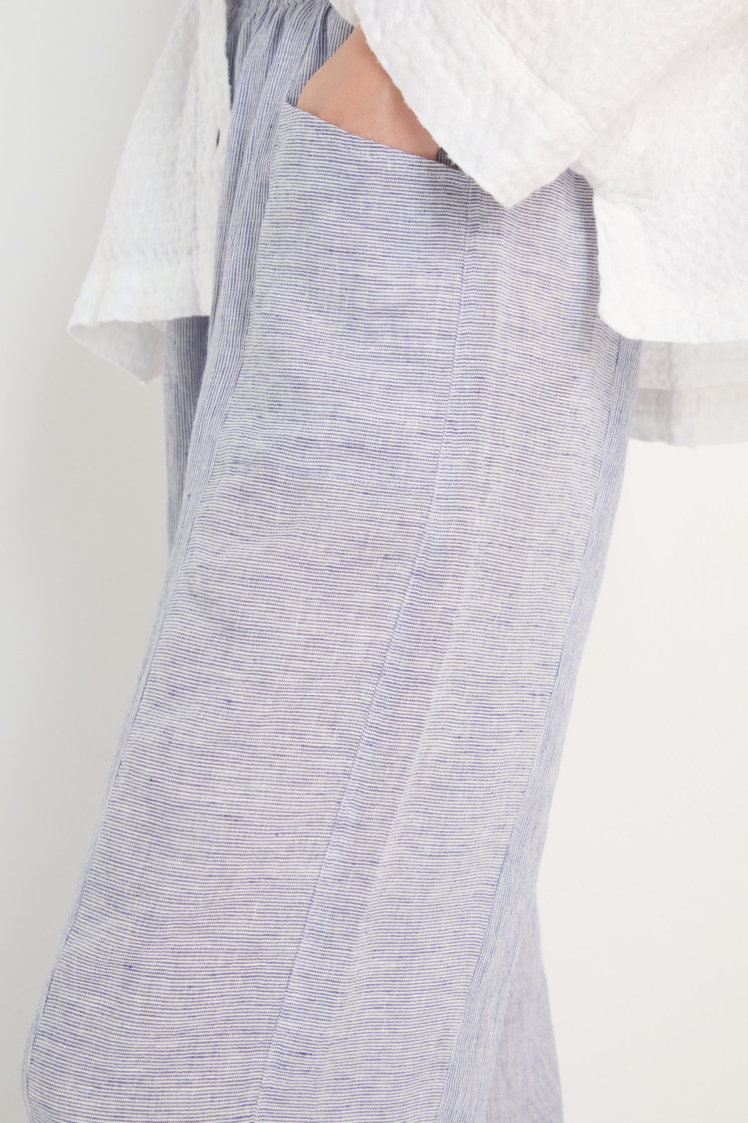 Close-up of a person wearing the Ticking Linen Stripe Bubble Trousers with an elasticated waist and a hand in the pocket, paired with a textured white top.