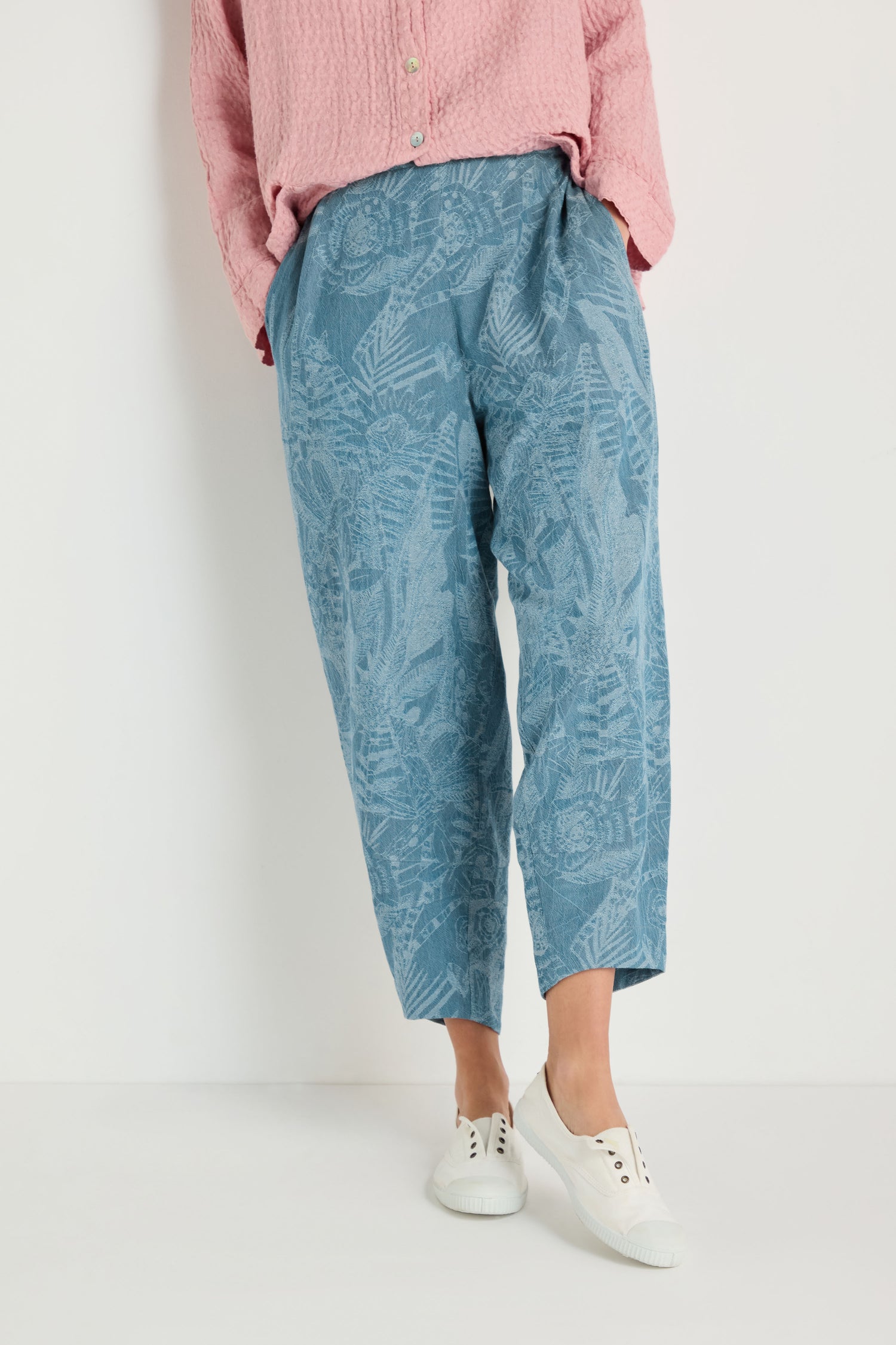 Person wears a pink textured shirt, Floral Jacquard Cotton Bubble Trouser in denim blue, and white sneakers, standing against a plain white background.