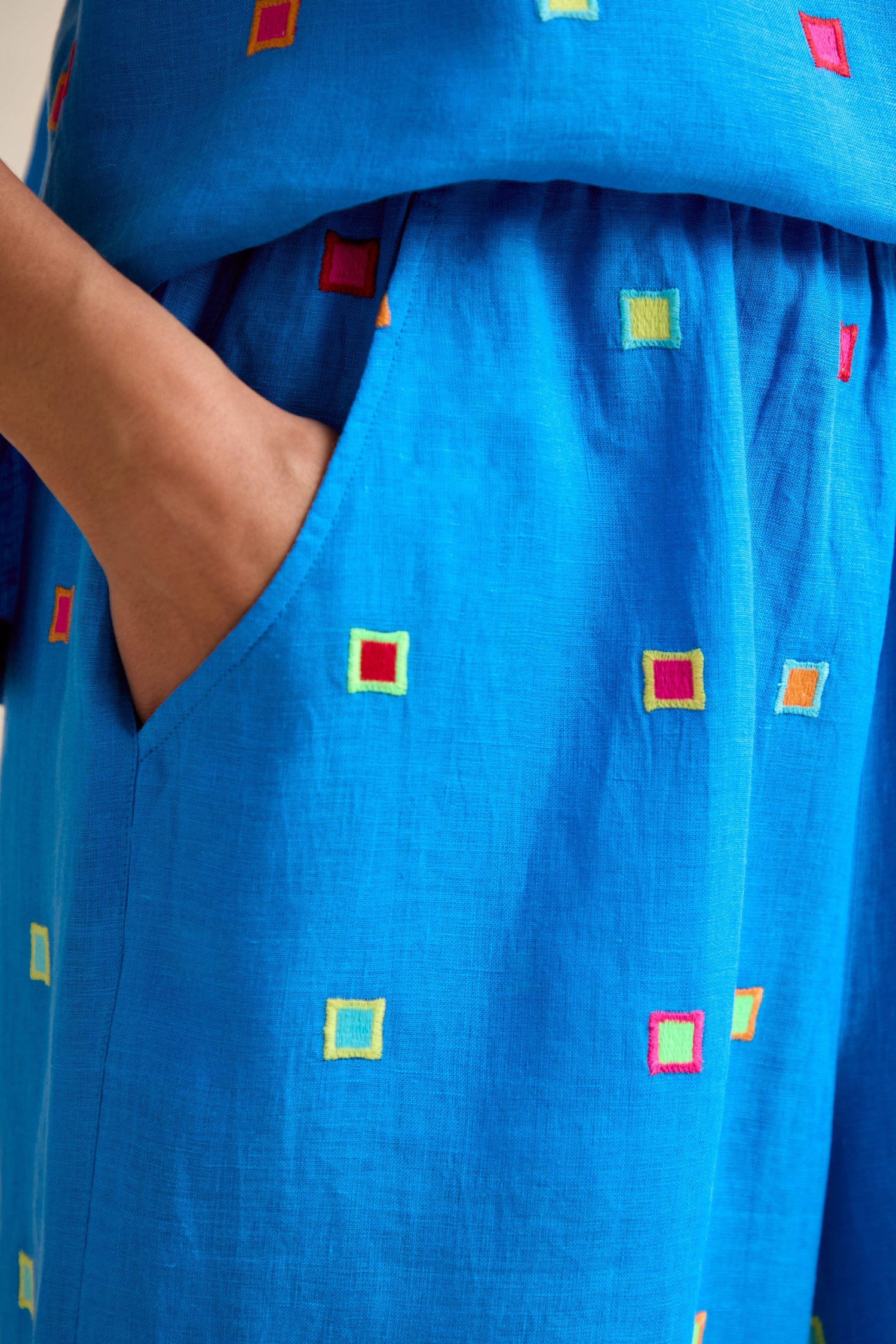 A close-up of a hand in the pocket of Embroidered Squares Linen Wide Trousers, featuring colorful embroidery, a wide fit, and a modern cropped length.