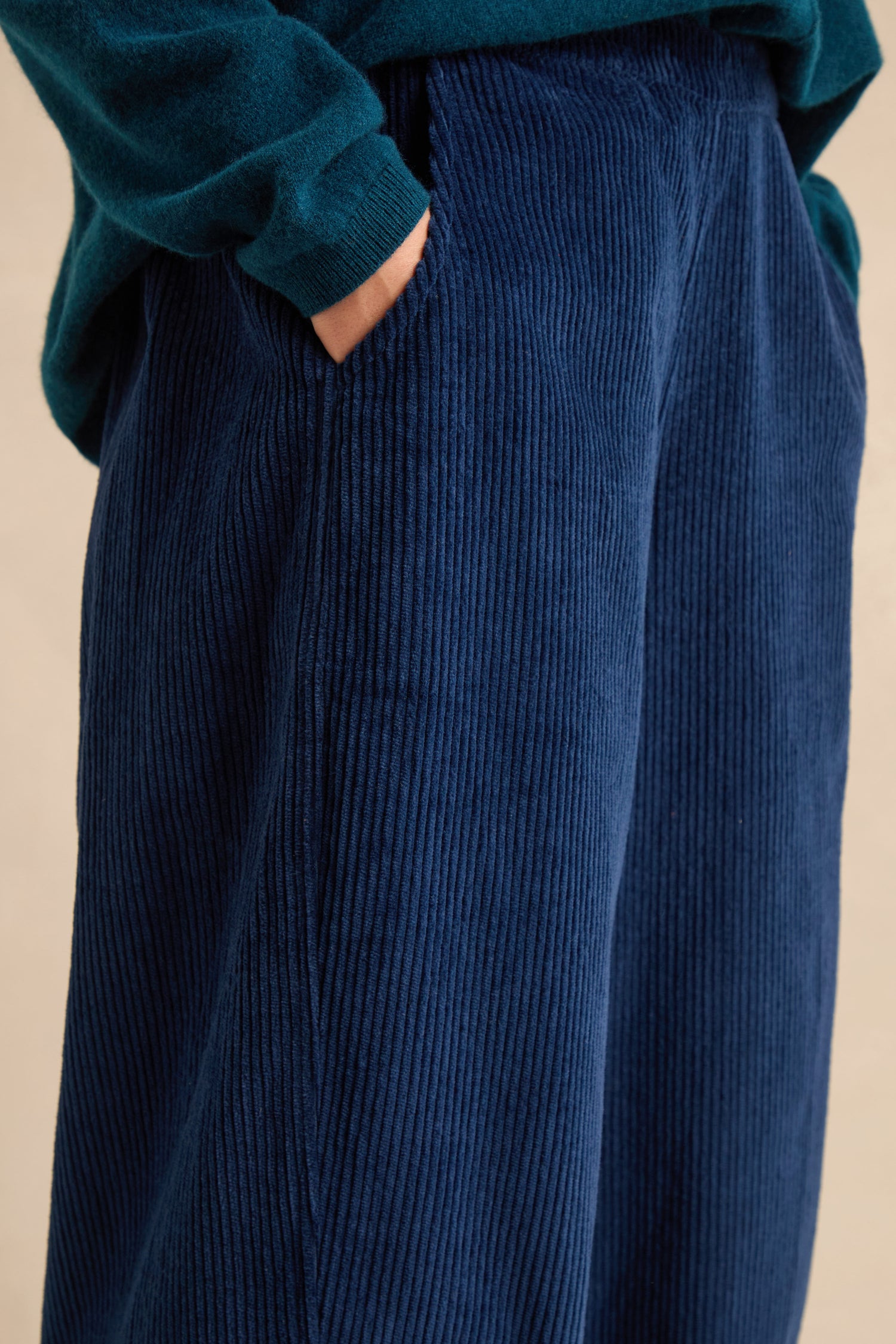 A person wearing the Marine Jumbo Cord Bubble Trousers in navy blue—crafted from pure cotton with a wide-leg fit—paired with a dark green top, one hand in pocket, photographed from the side.