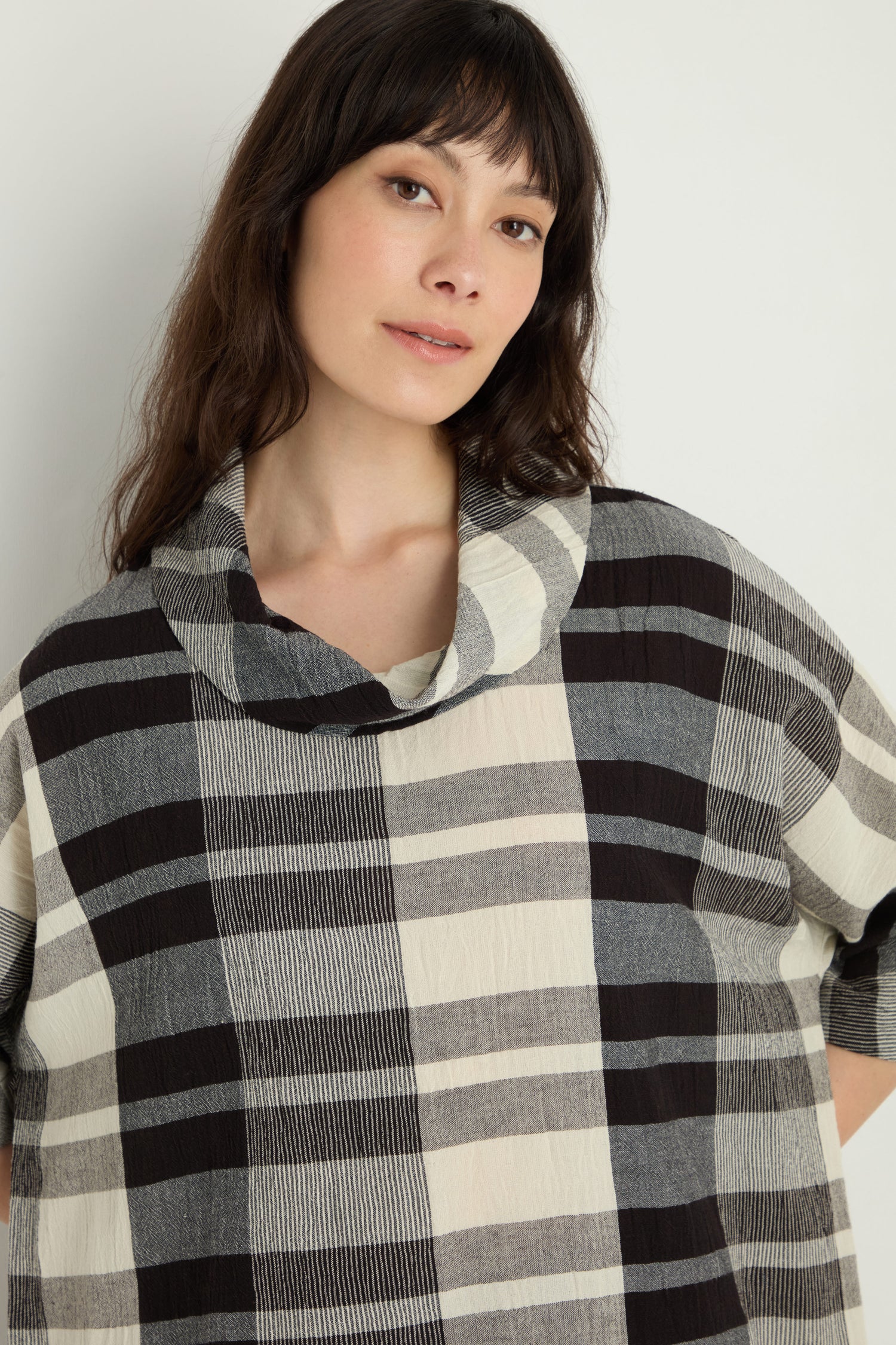 A woman with long brown hair wears the Monochrome Crinkle Check Cowl Neck Top, standing against a plain light background.