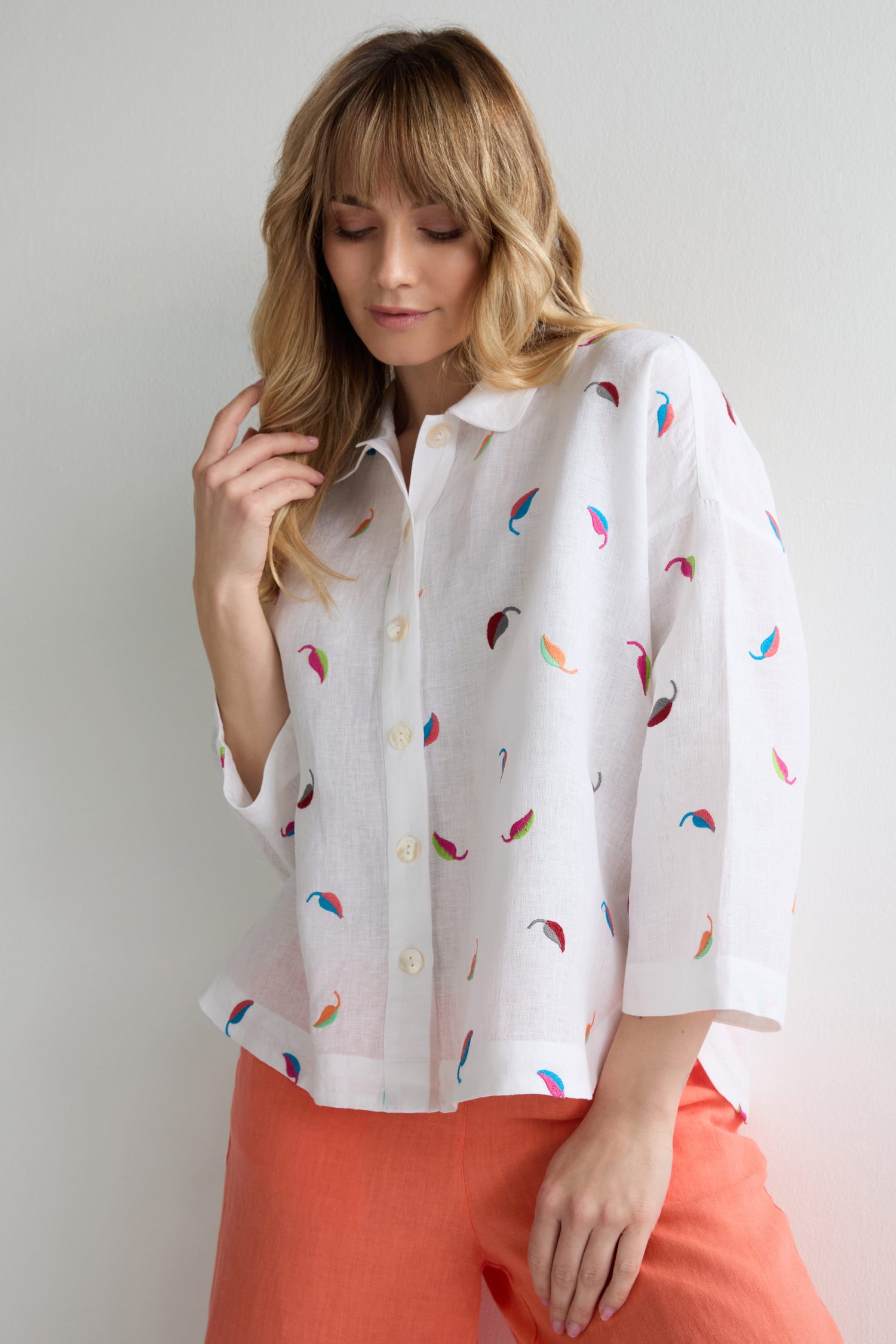 Woman wearing the Embroidered Leaf Boxy Shirt with coral pants, standing against a plain light background.