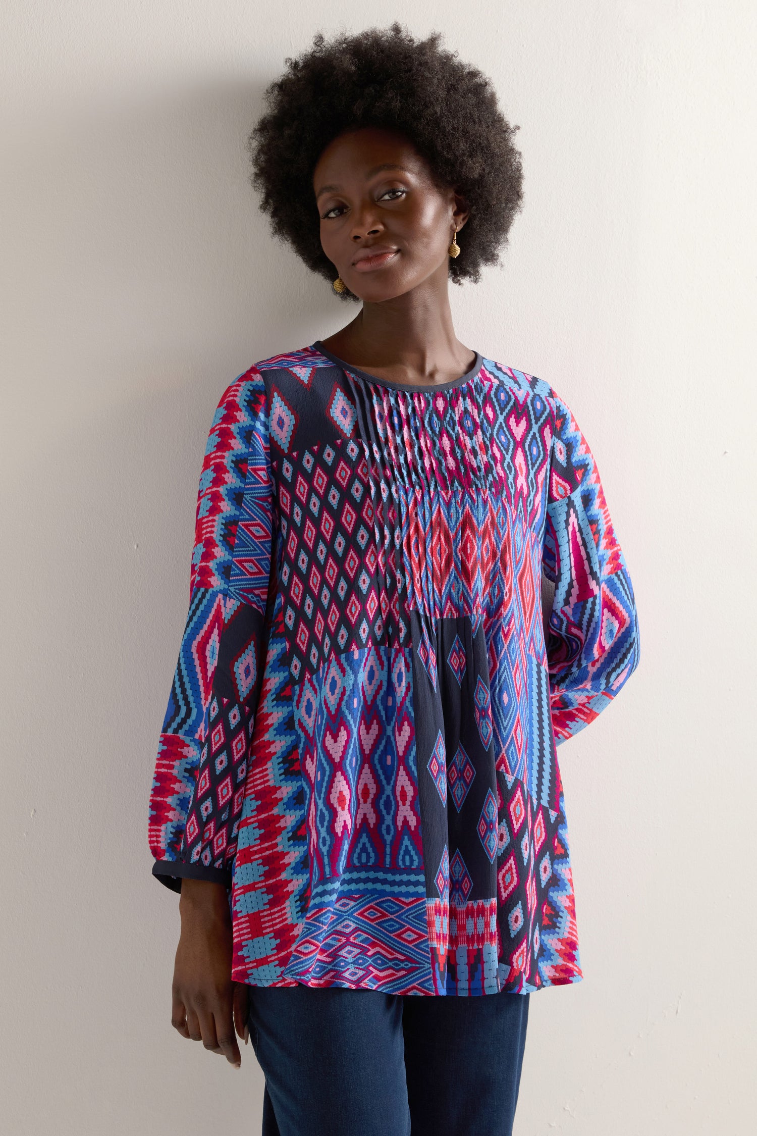 The woman confidently poses against a plain backdrop, wearing a vibrant Diamond Geo Patchwork Top.