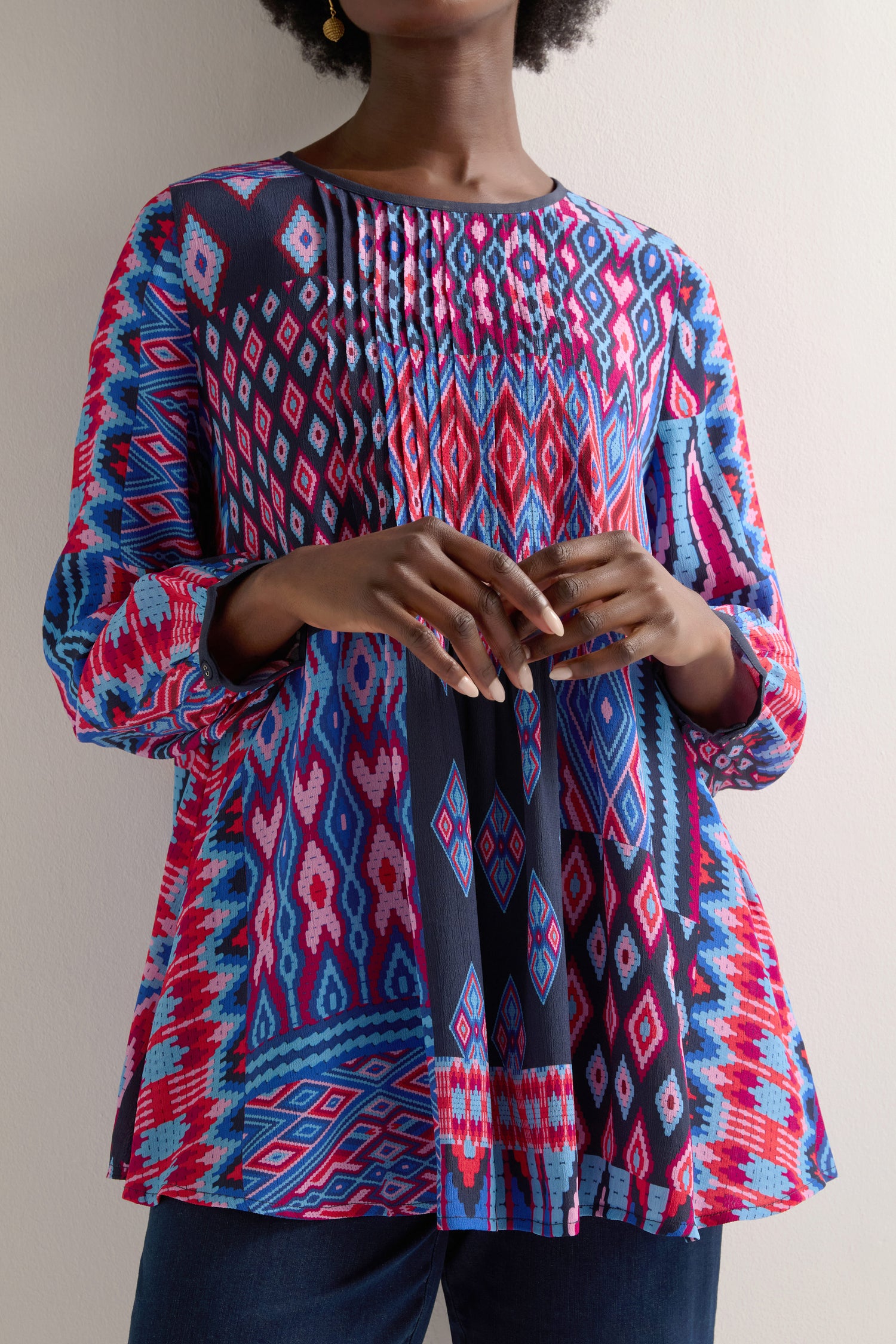 A person in a vibrant Diamond Geo Patchwork Top, featuring long sleeves, stands against a plain backdrop.