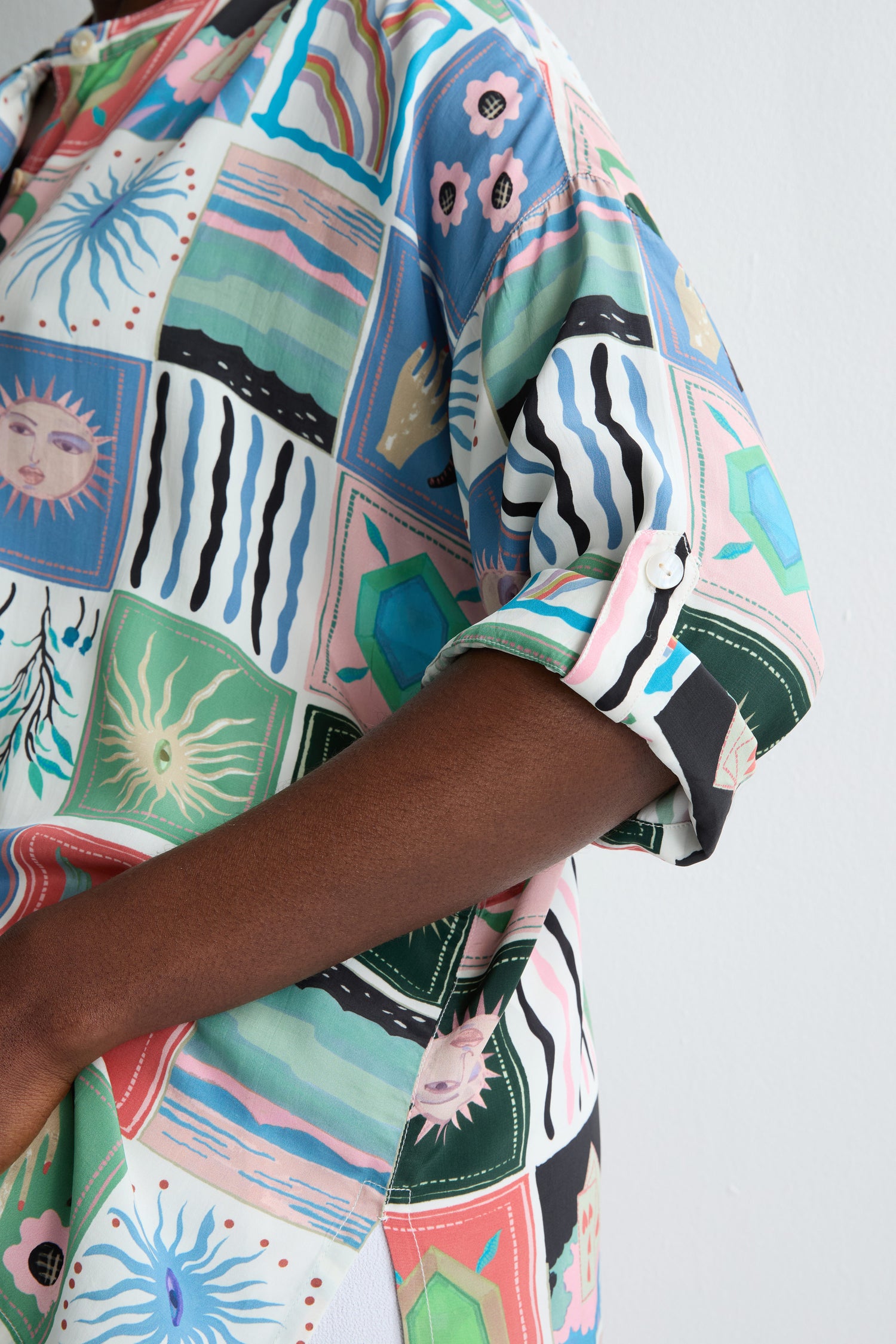 Someone wearing the Mystical Collage Boxy Shirt, featuring a relaxed boxy fit, rolled-up sleeves, a mandarin collar, and adorned with abstract and celestial patterns.