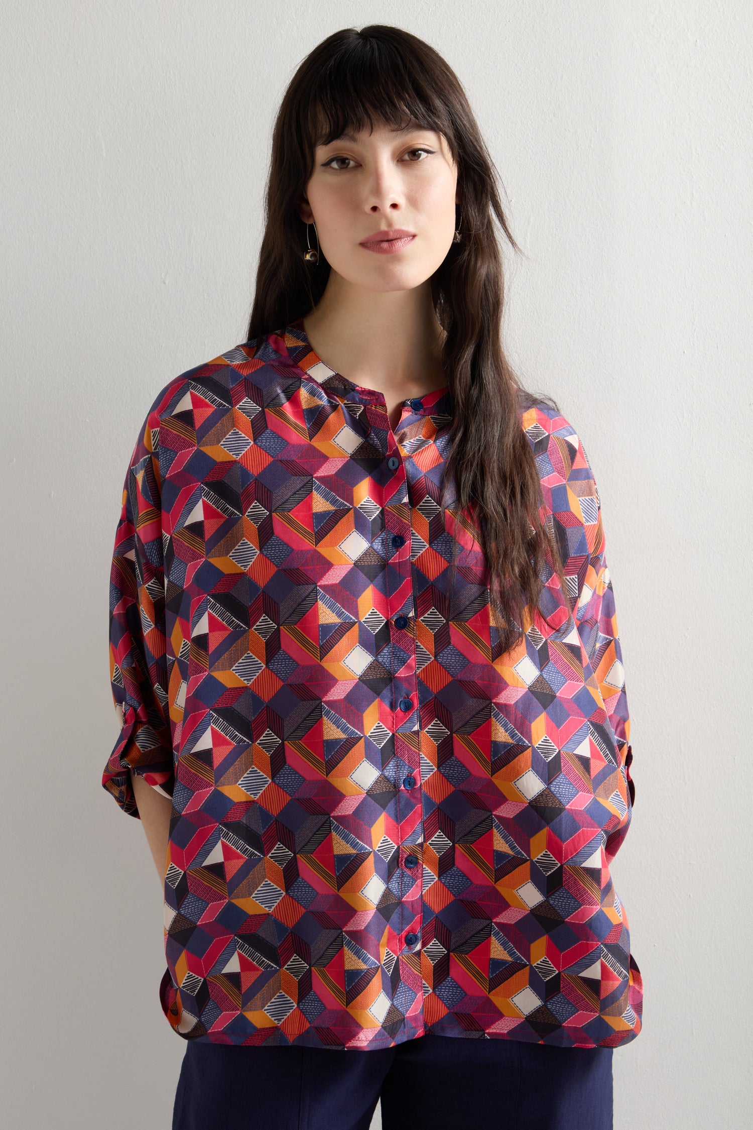 A woman stands against a plain light background, wearing an oversized fit Small Stitched Squares Silk Shirt.