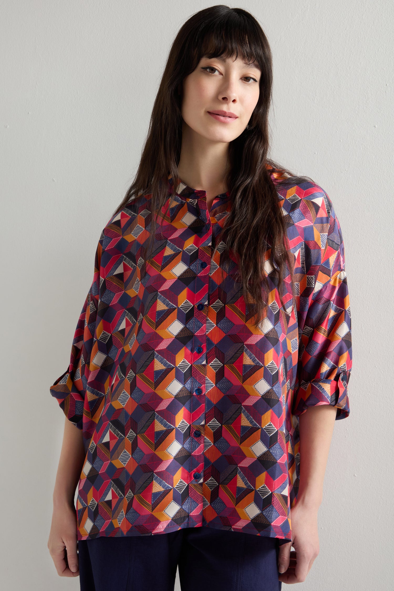 Wearing a Small Stitched Squares Silk Shirt with a colorful geometric square print, a person stands against a plain background, looking slightly to the side.