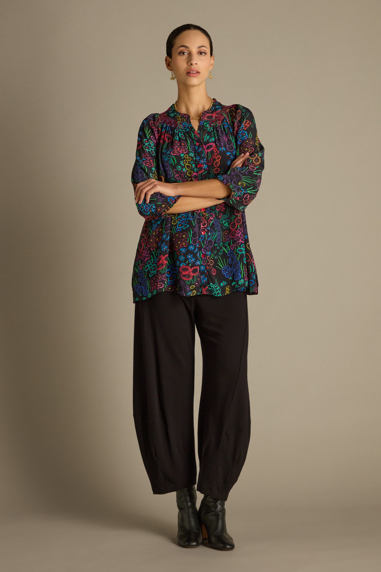 Against a plain backdrop, a person stands wearing a vibrant Floral Embroidery Print Shirt, paired elegantly with black pants and matching boots.