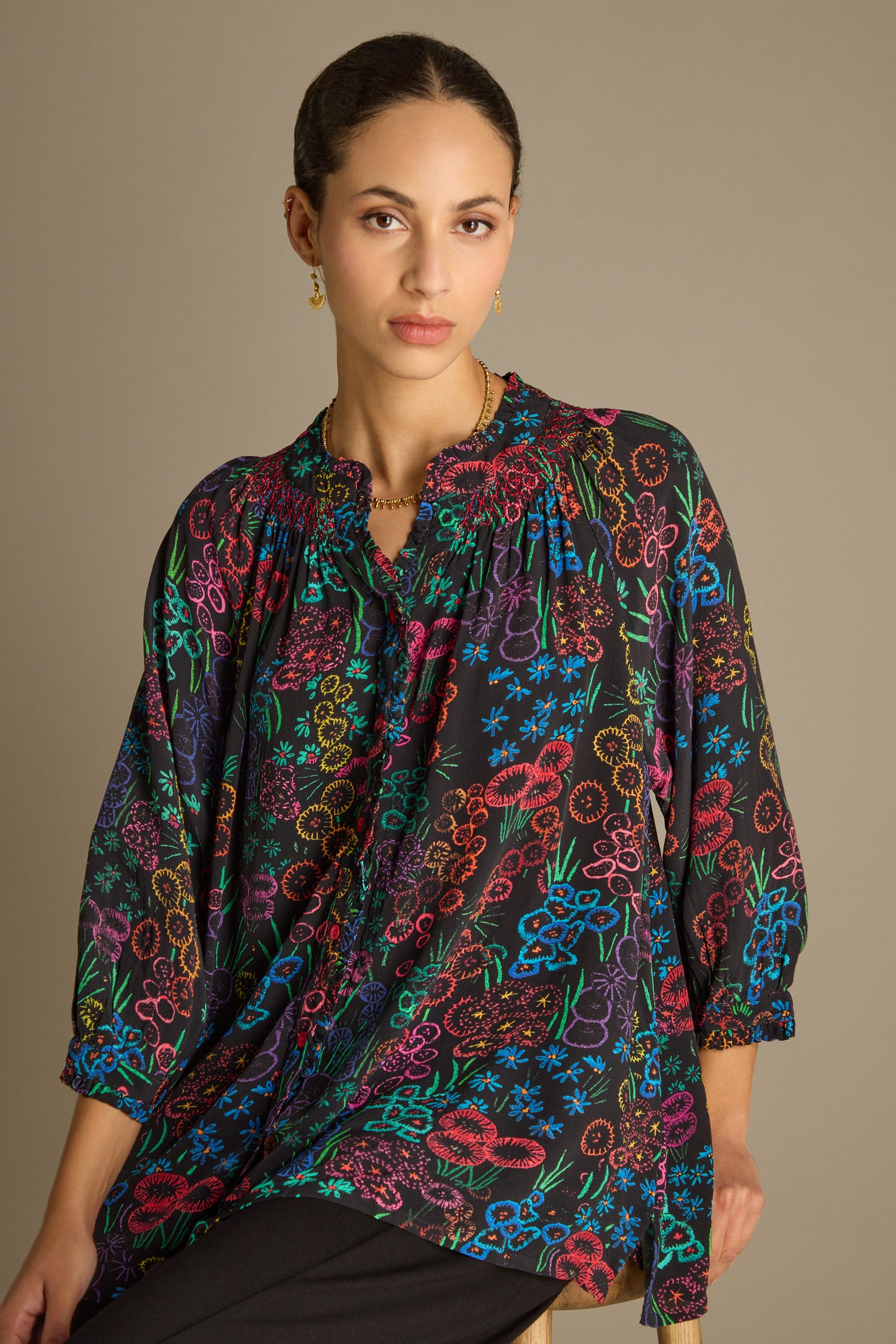 A person wearing a vibrant Floral Embroidery Print Shirt sits gracefully against a neutral background, highlighting exquisite artisanal craftsmanship.