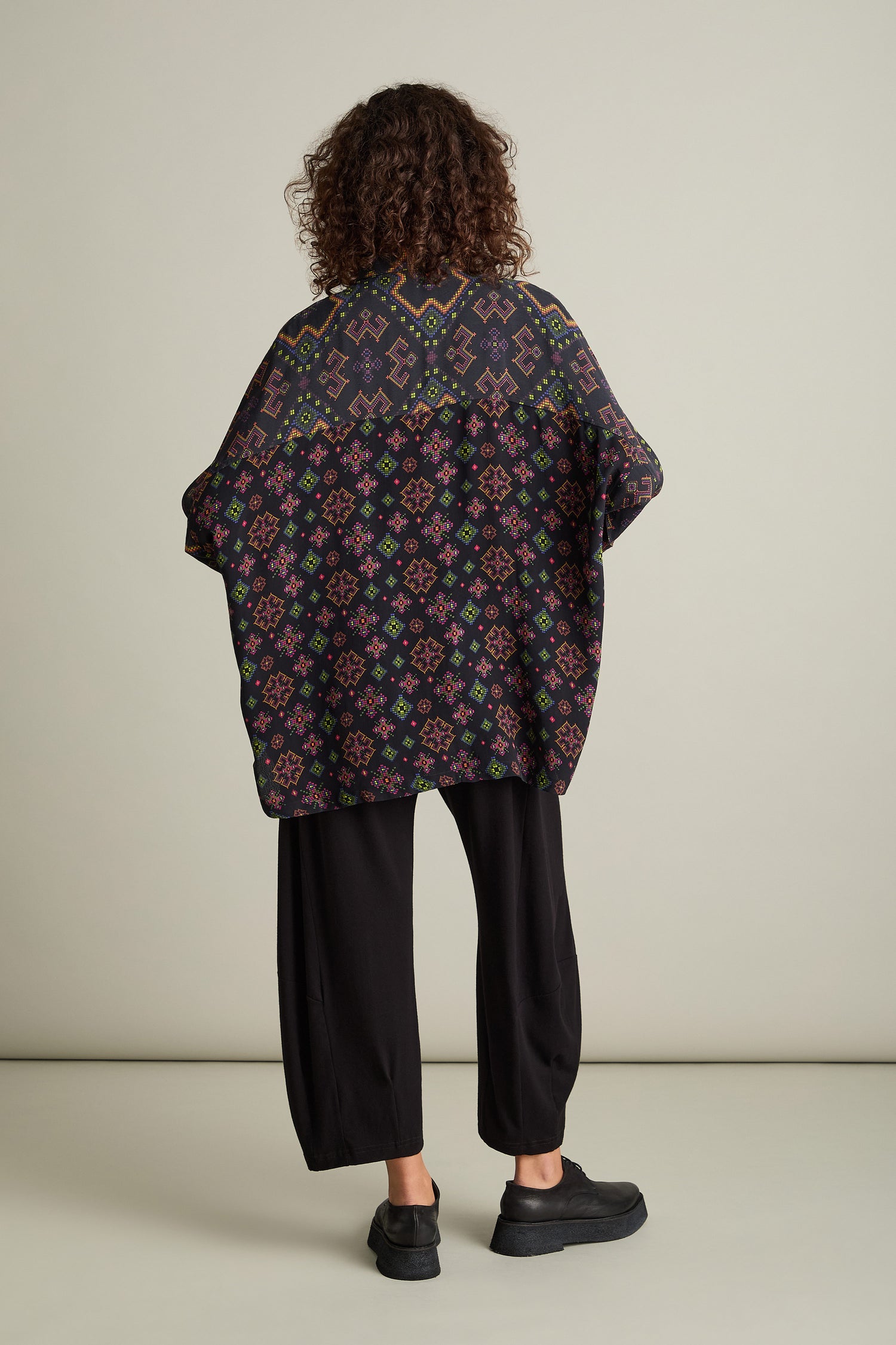 A person stands against a plain backdrop, wearing a Pixelated Jacquard Print Shirt with an oversized boxy fit in black and matching loose black pants. The person's back is facing the camera.