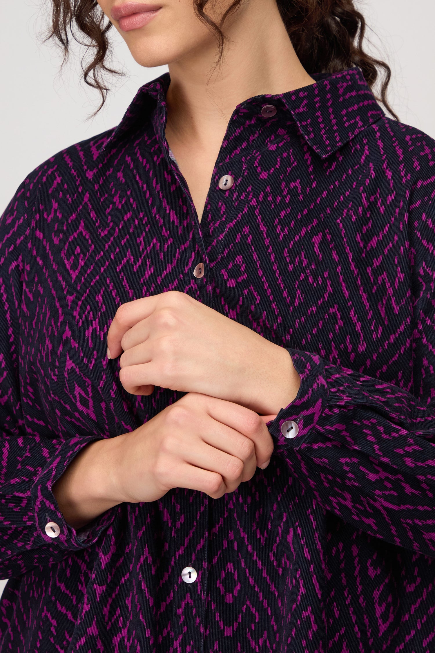 A person wearing the Ornate Textured Night and Plum Cord Shirt, with hands gently clasped near their chest.