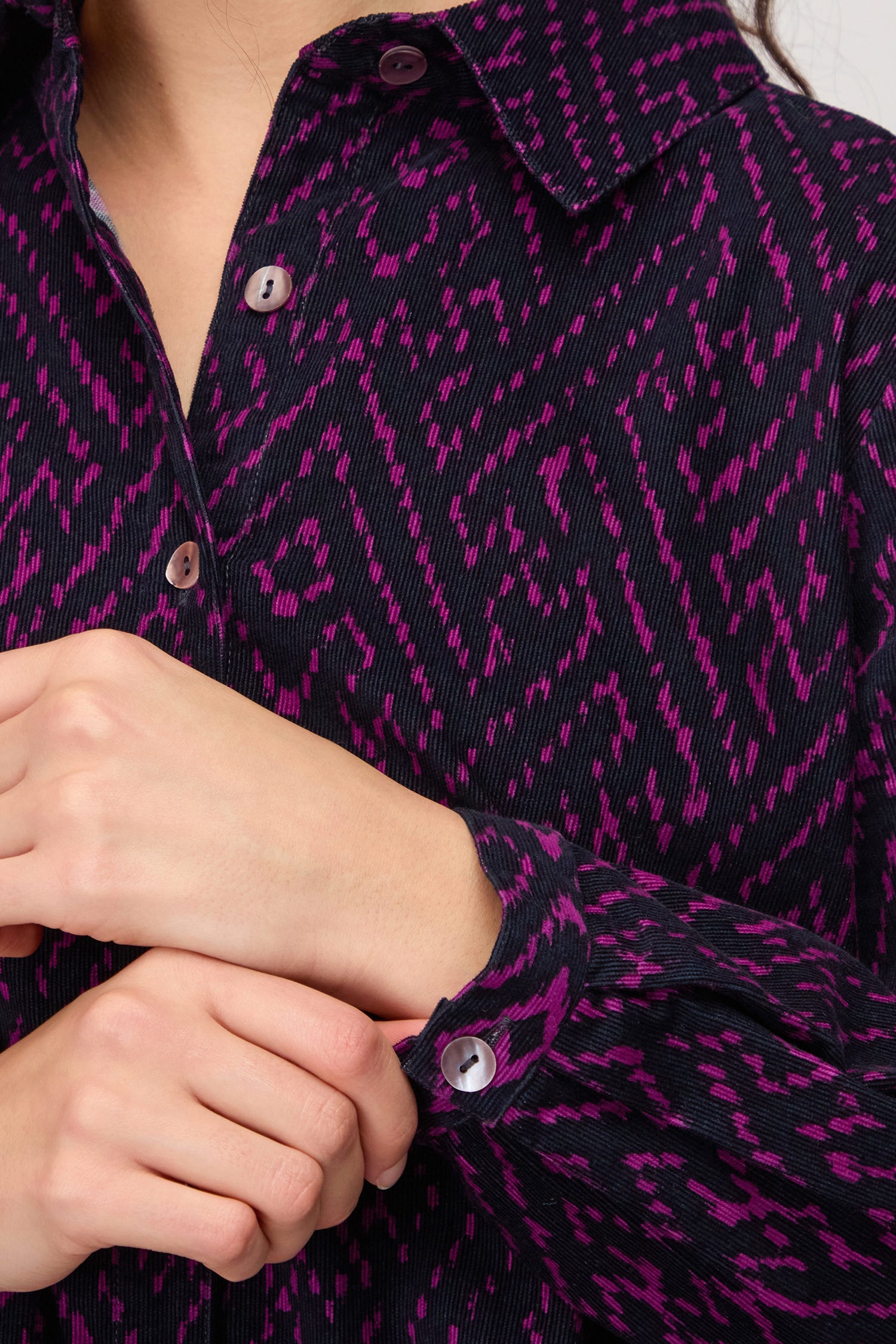 A person buttoning the cuff of the Ornate Textured Night and Plum Cord Shirt, featuring a relaxed cut and purple geometric pattern.