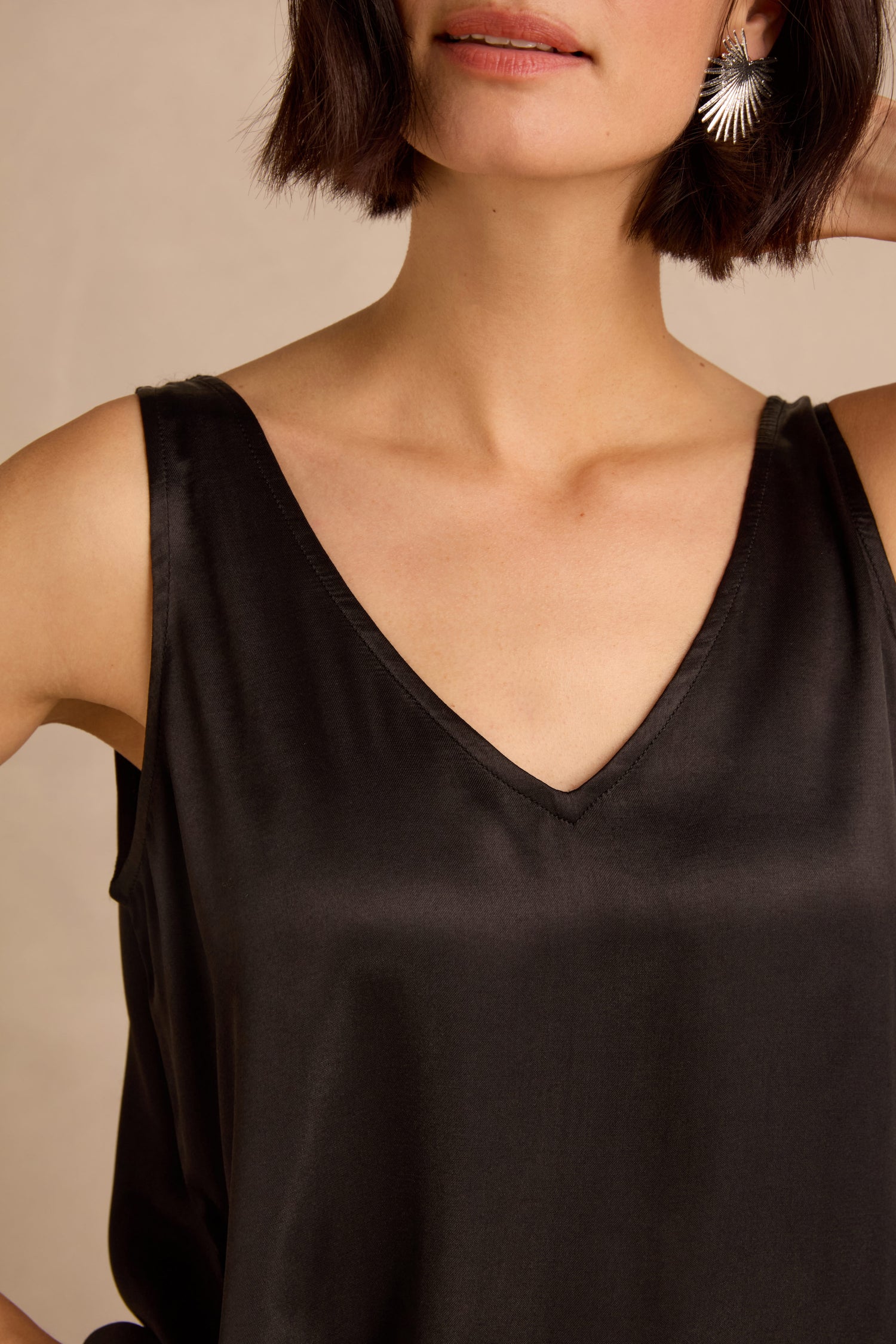 Woman wearing a sleeveless black Cupro Layering Vest and silver sunburst earrings, posing with one arm bent and her hand behind her head.