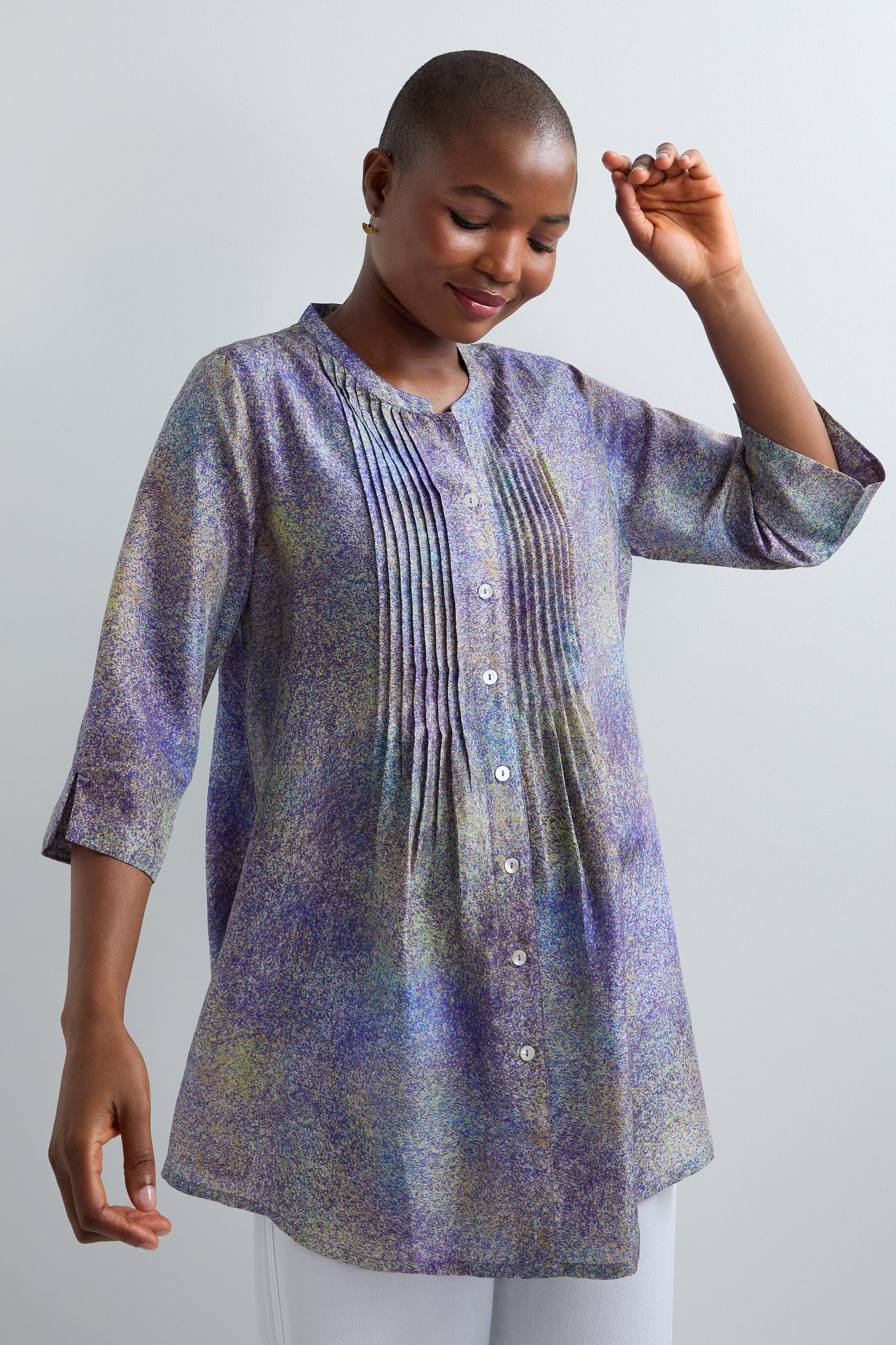A person wearing the Abstract Speckled Silk Shirt, a classic fit, long-sleeved tunic with pleats, front buttons, a stand collar, and a multicolored abstract speckled design, stands against a plain light background.