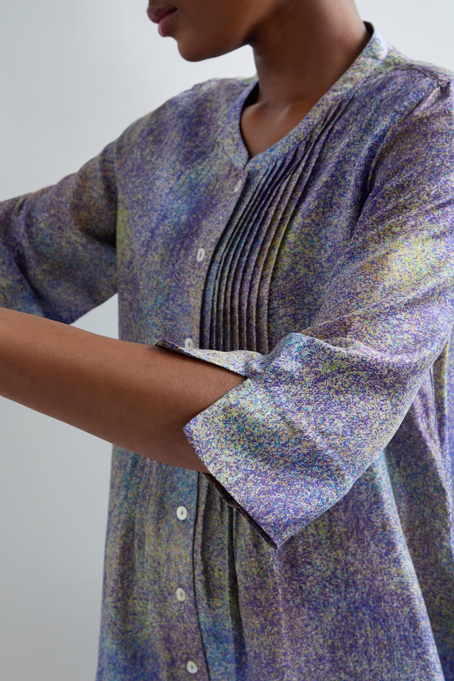 A person wearing the Abstract Speckled Silk Shirt, featuring chest pleats, white buttons, rolled-up sleeves, and a flattering fit-and-flare shape.